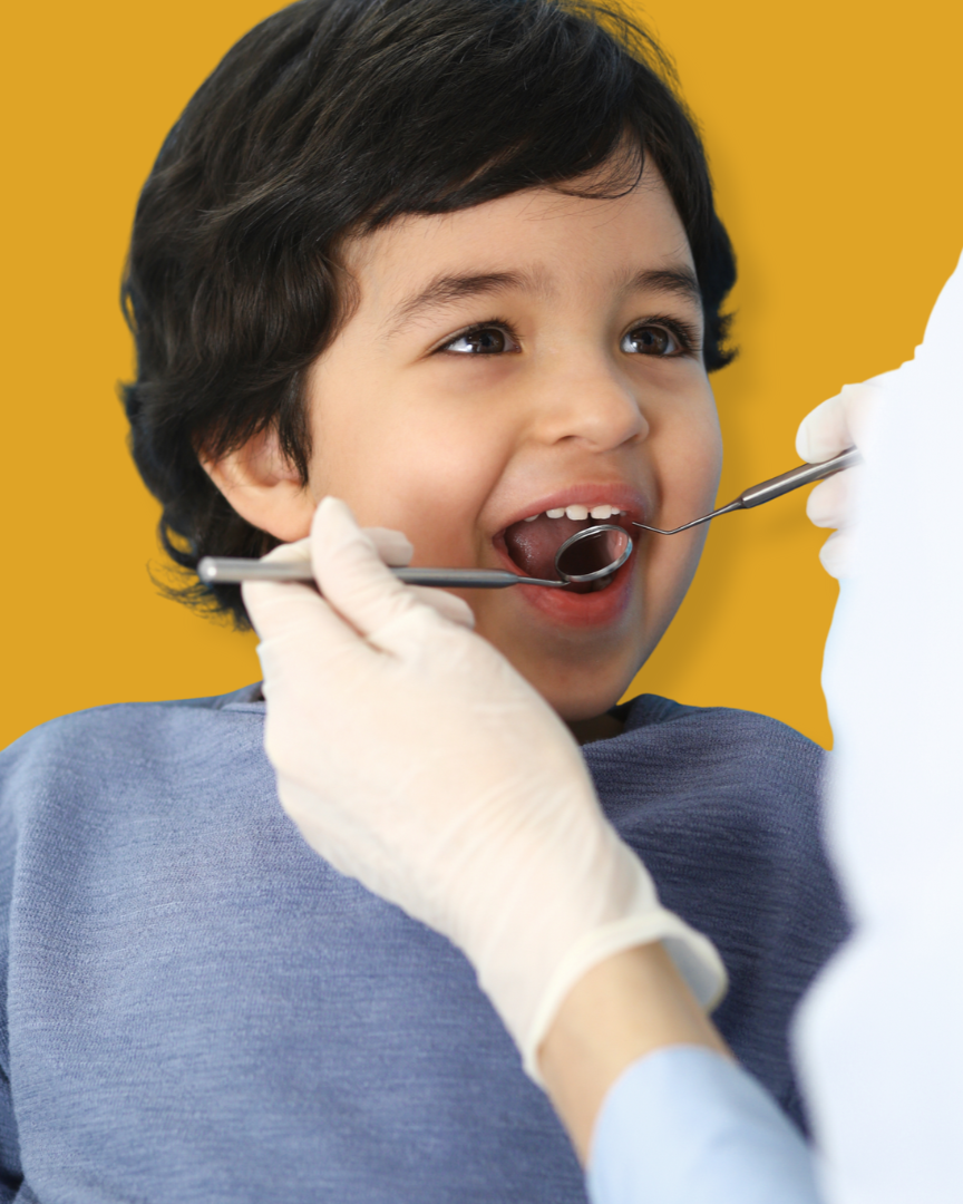 A young boy at the dentist's office with his mouth open, while a dentist or dental hygienist examines his teeth with dental tools. The background is bright yellow.