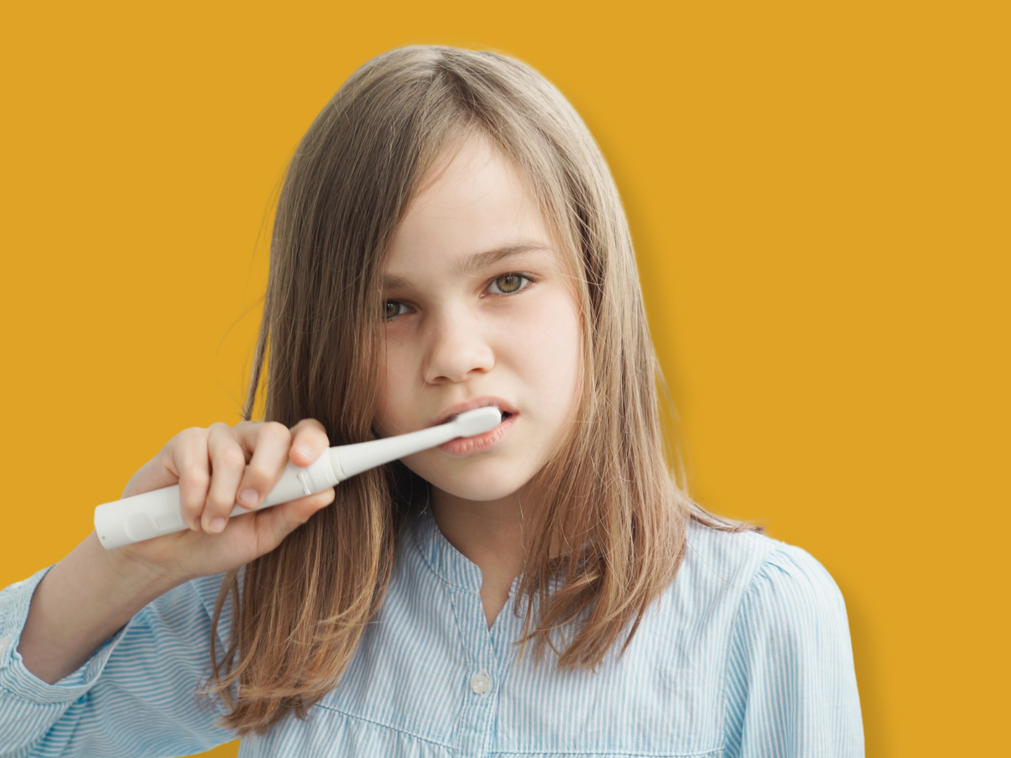 A young girl with long brown hair brushes her teeth with a white electric toothbrush against a solid yellow background.