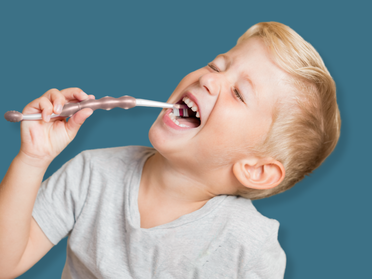 Young boy with blonde hair brushing his teeth with a toothbrush against a blue background.