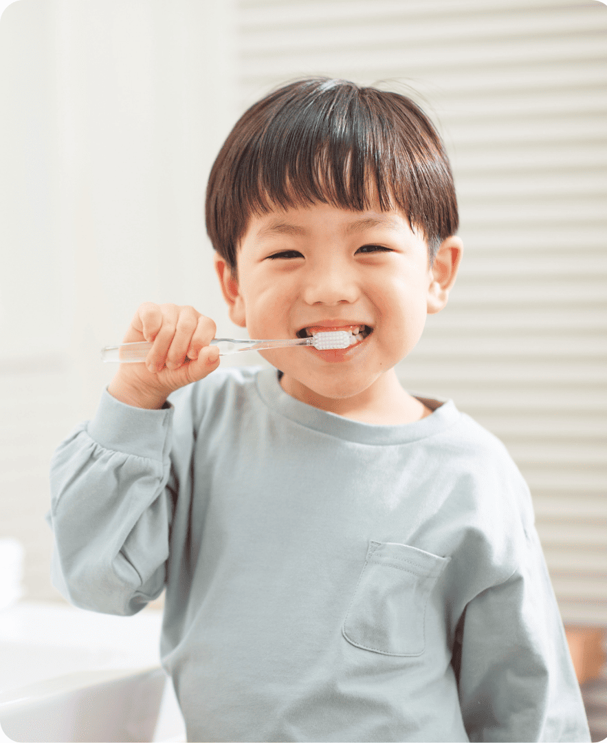 A young boy brushing his teeth and smiling in a bright bathroom.