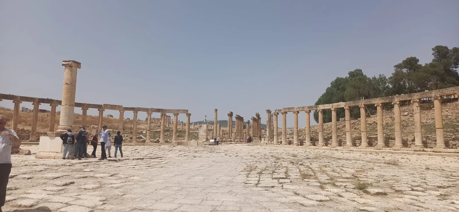 Ancient ruins with columns and stone pavement, tourists exploring the site under a clear sky.