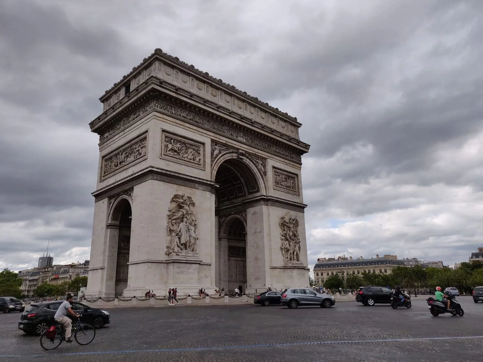 The Arc de Triomphe in Paris, France, under a cloudy sky, with cars and people on the street.