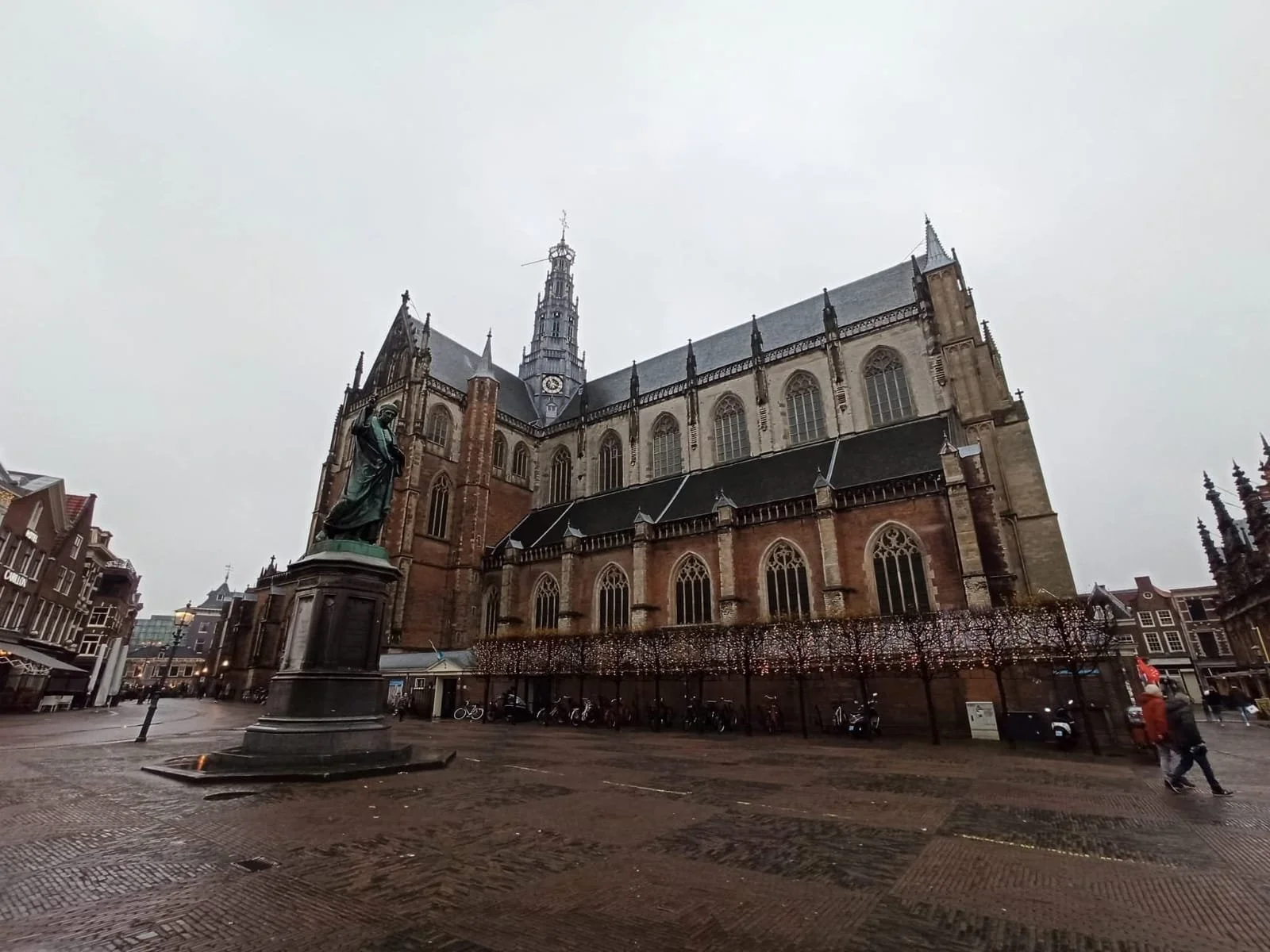 A large Gothic-style church with stained glass windows and detailed stonework, situated on a cobblestone square with a statue of a historical figure in front.