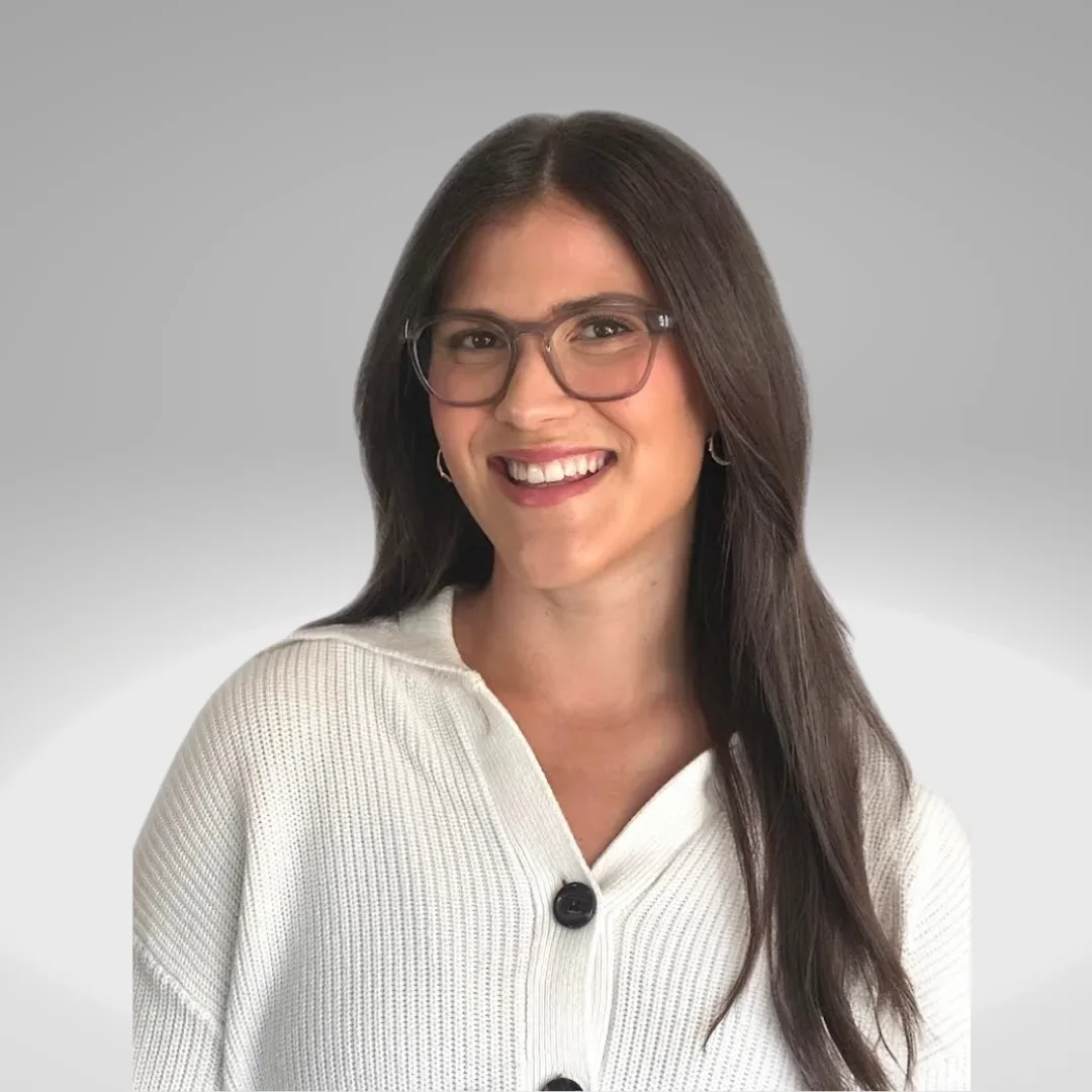 A woman with long dark hair, wearing glasses, earrings, and a white sweater, smiling at the camera with a gray gradient background.