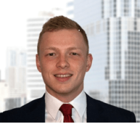 Portrait of a young man in a suit and tie, smiling, with a cityscape background.