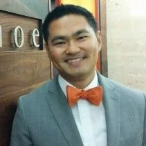 Man wearing a grey suit with an orange bow tie, smiling.