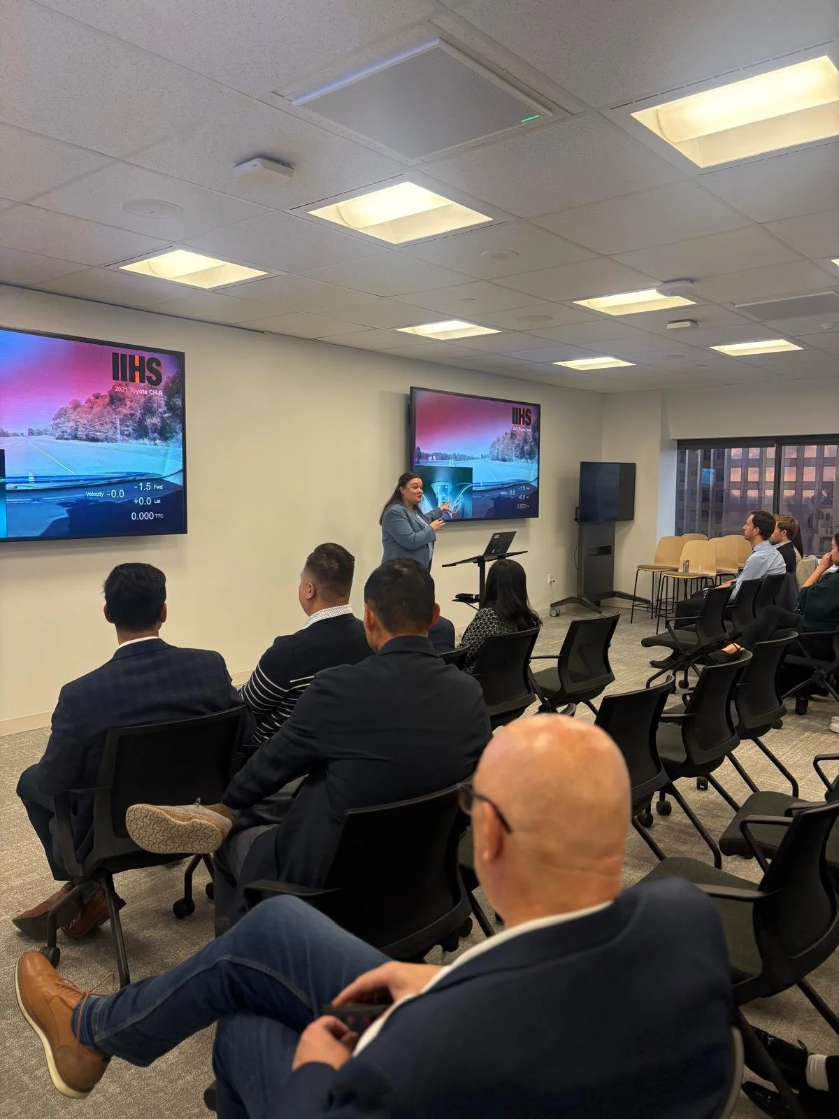 A woman giving a presentation to a group of people in a conference room with two large screens displaying a boat and water scene.