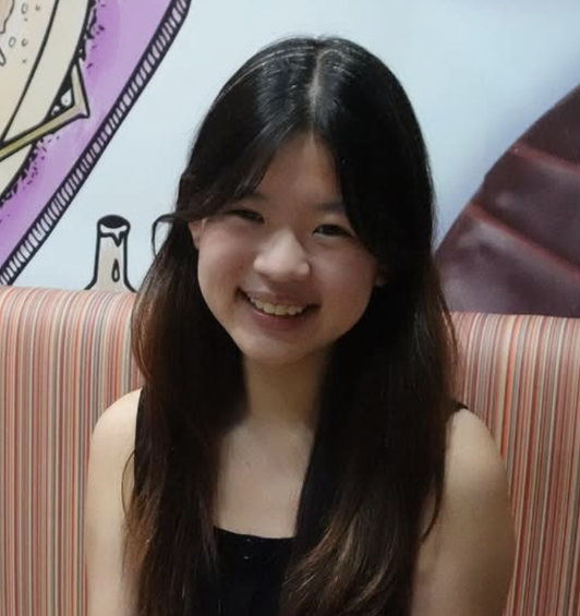Young woman with long dark hair smiling and sitting on striped upholstery in front of colorful wall art.