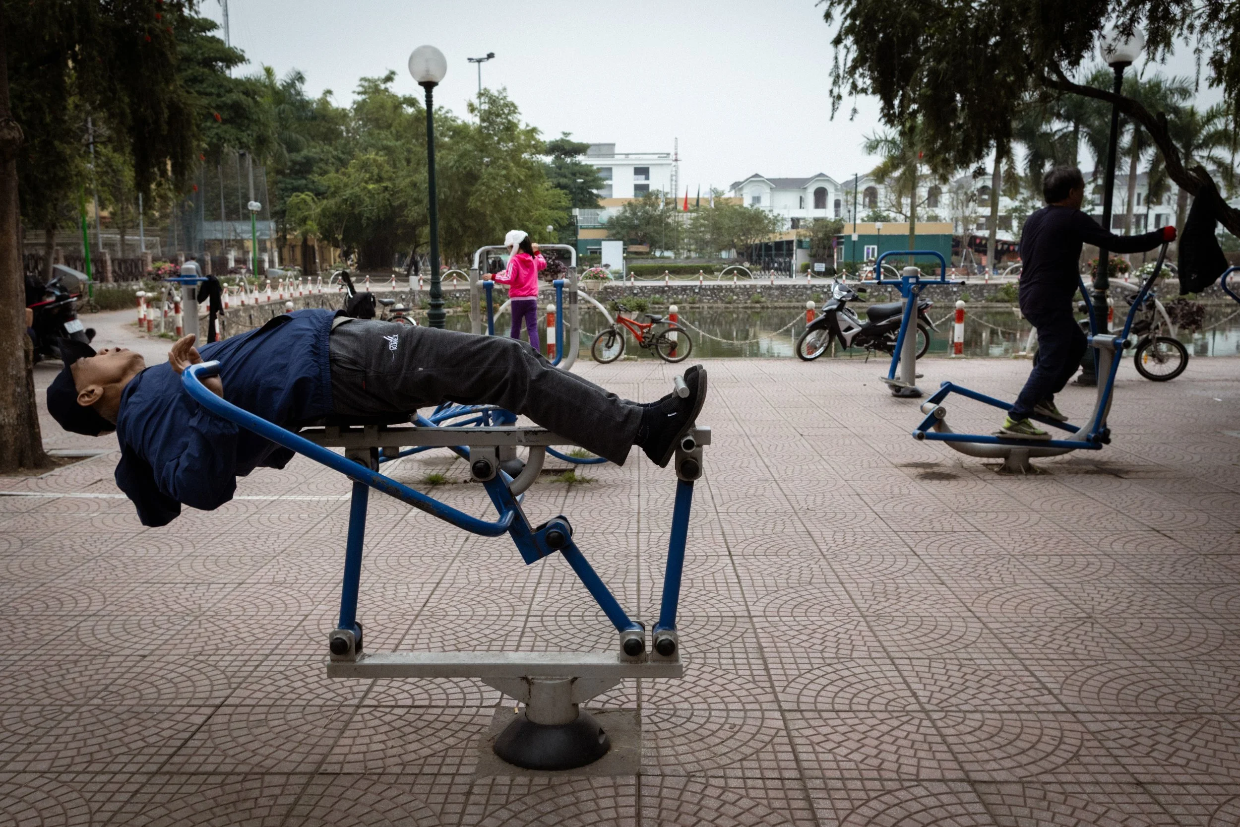 Locals enjoy the morning while using outdoor exercise equipment. Hanoi, Vietnam, 2019