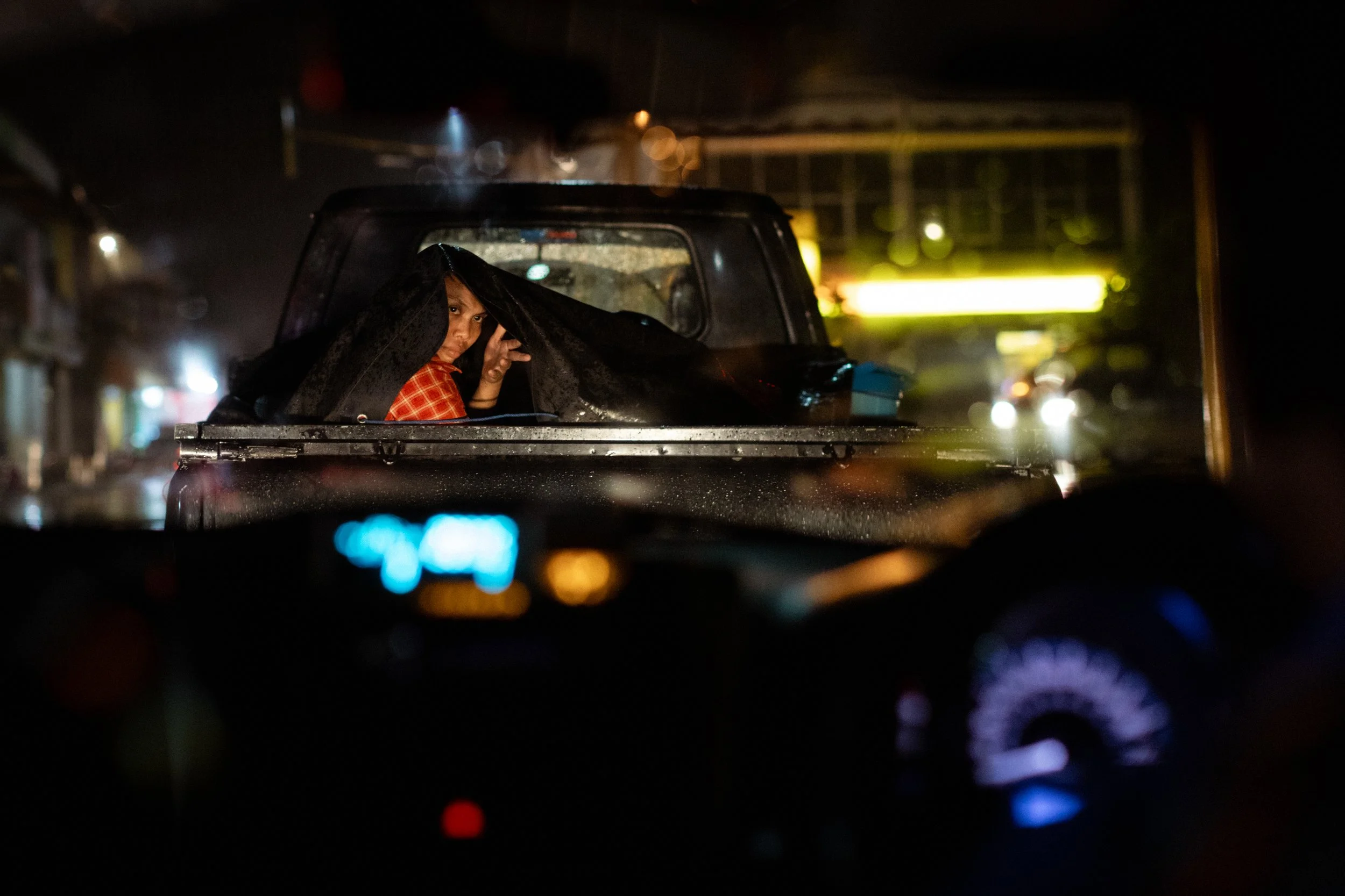 A woman shelters from the rain under a tarp on the back of a pickup. Lombok, Indonesia, 2017
