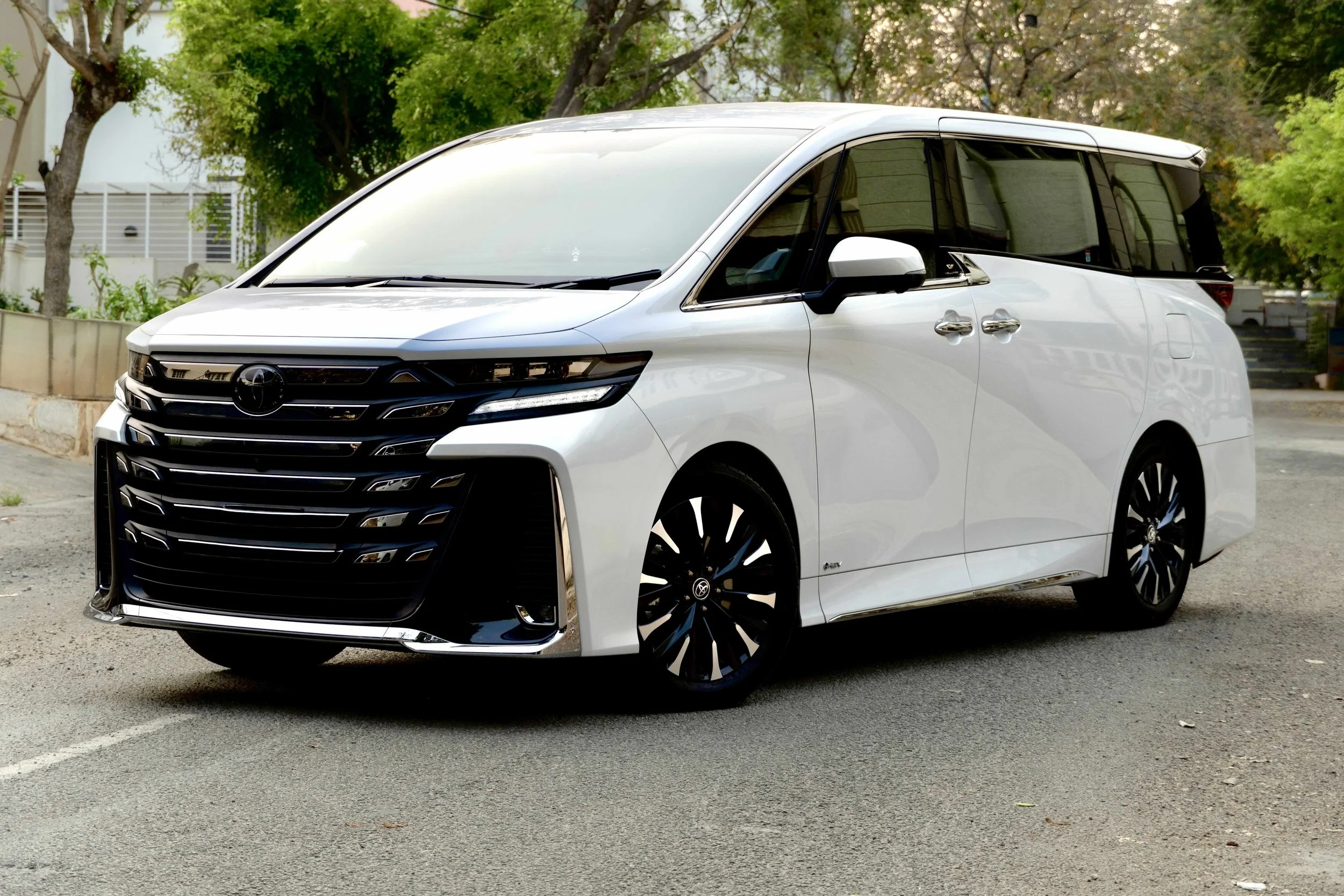 a new white color Toyota Vellfire standing on a road with tress in the background