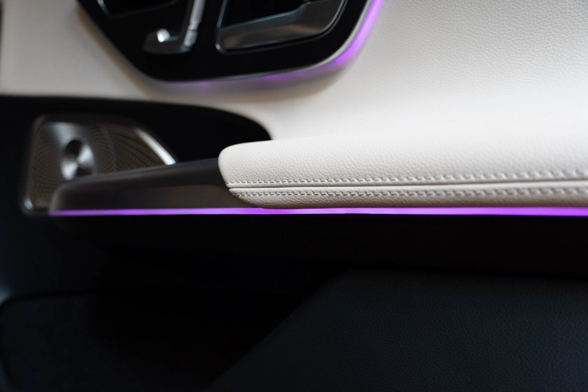 Close-up of the interior dashboard of a modern car, showing part of the dashboard with purple accent lighting and a white leather armrest.