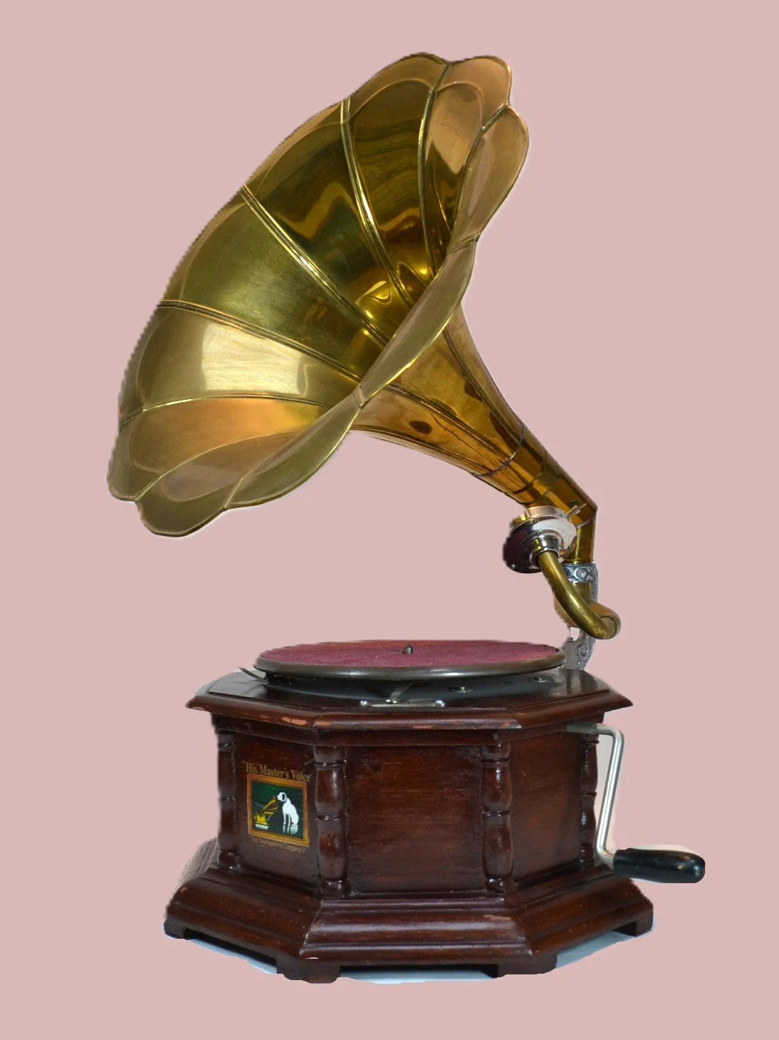 An antique gramophone with a brass horn and wooden base, set against a plain pink background.