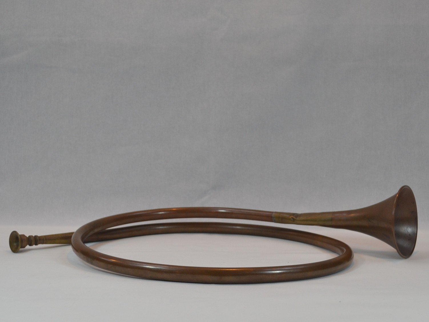 A vintage brass horn with a curved body and a flared opening, laying on a flat surface against a plain background.