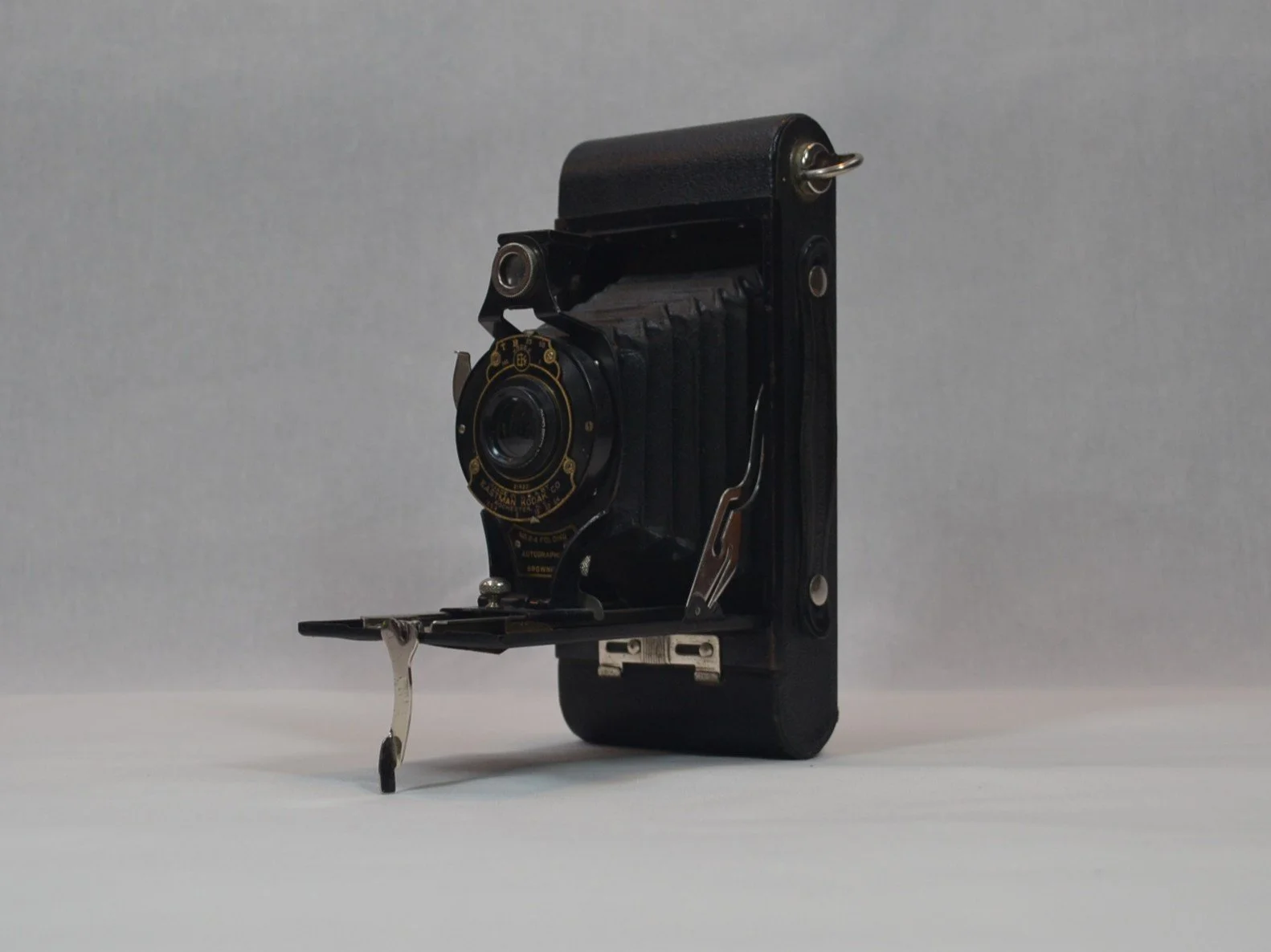 A vintage folding camera with a black body and metal details, set on a plain surface against a light grey background.