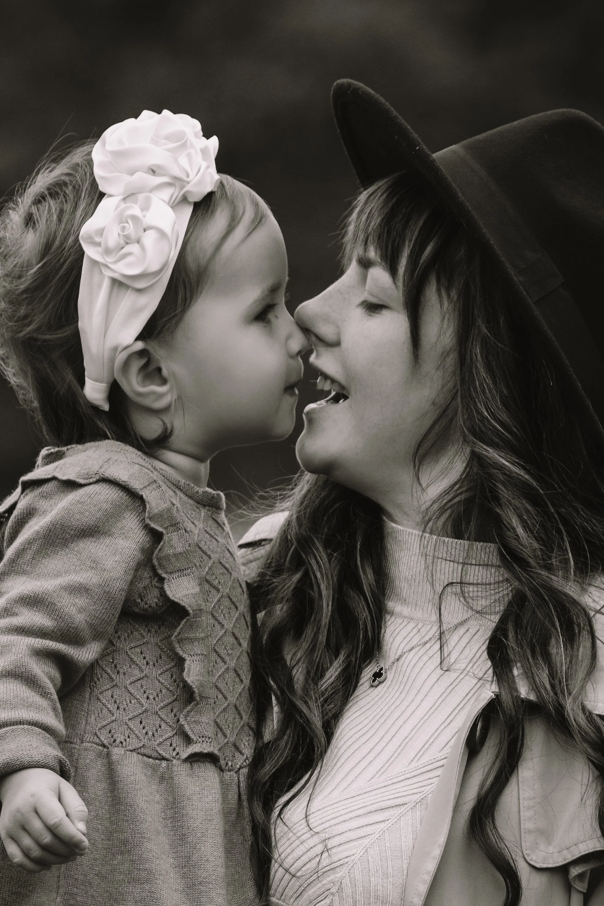 Ein junges Mädchen und eine Frau mit einem Hut berühren sich mit der Nase und drücken ihre Gesichter eng zusammen, in einer liebevollen Geste.