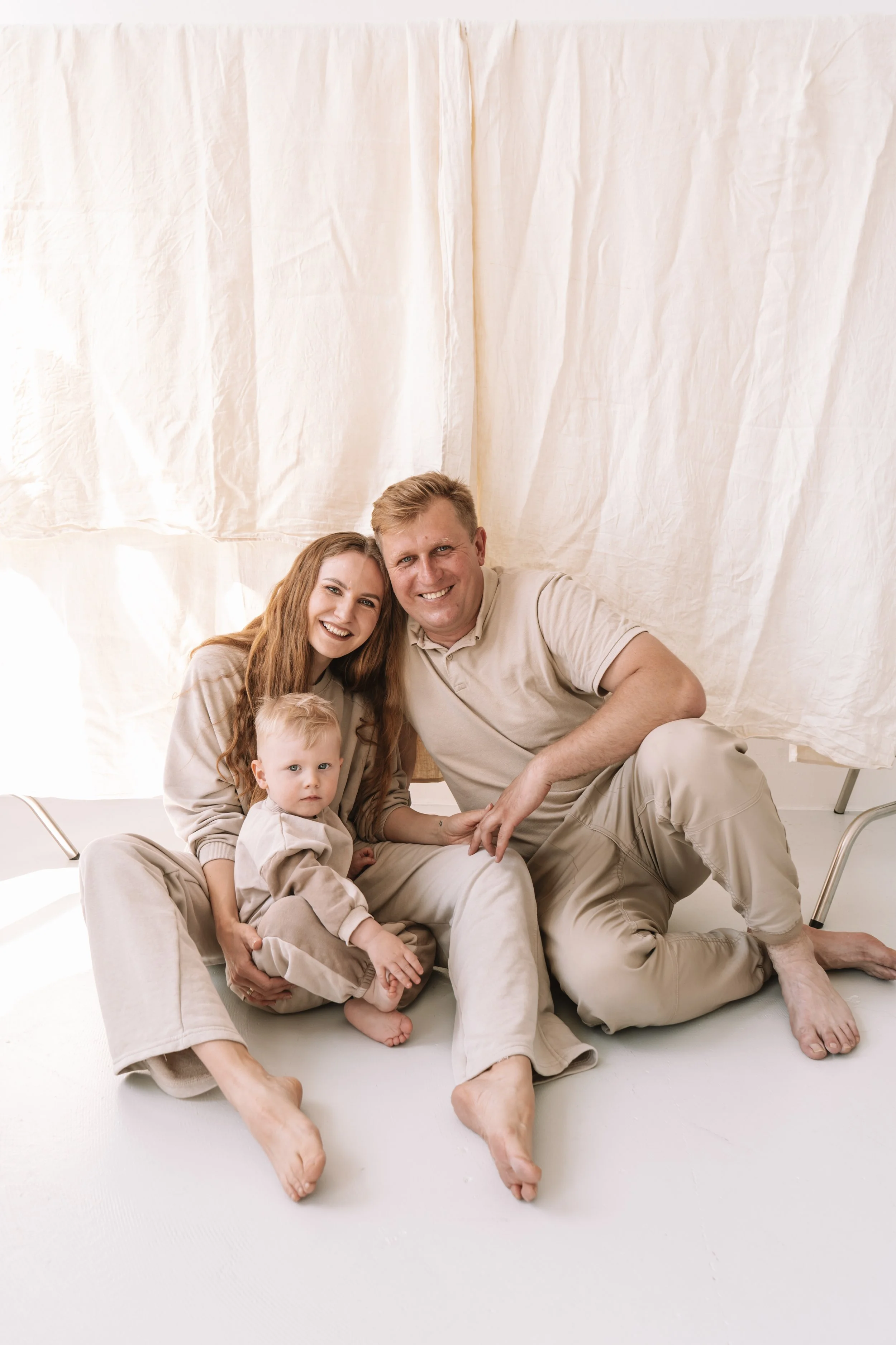 Familie sitzt auf dem Boden vor einem hellen Hintergrund, lächelnd für ein Portrait.