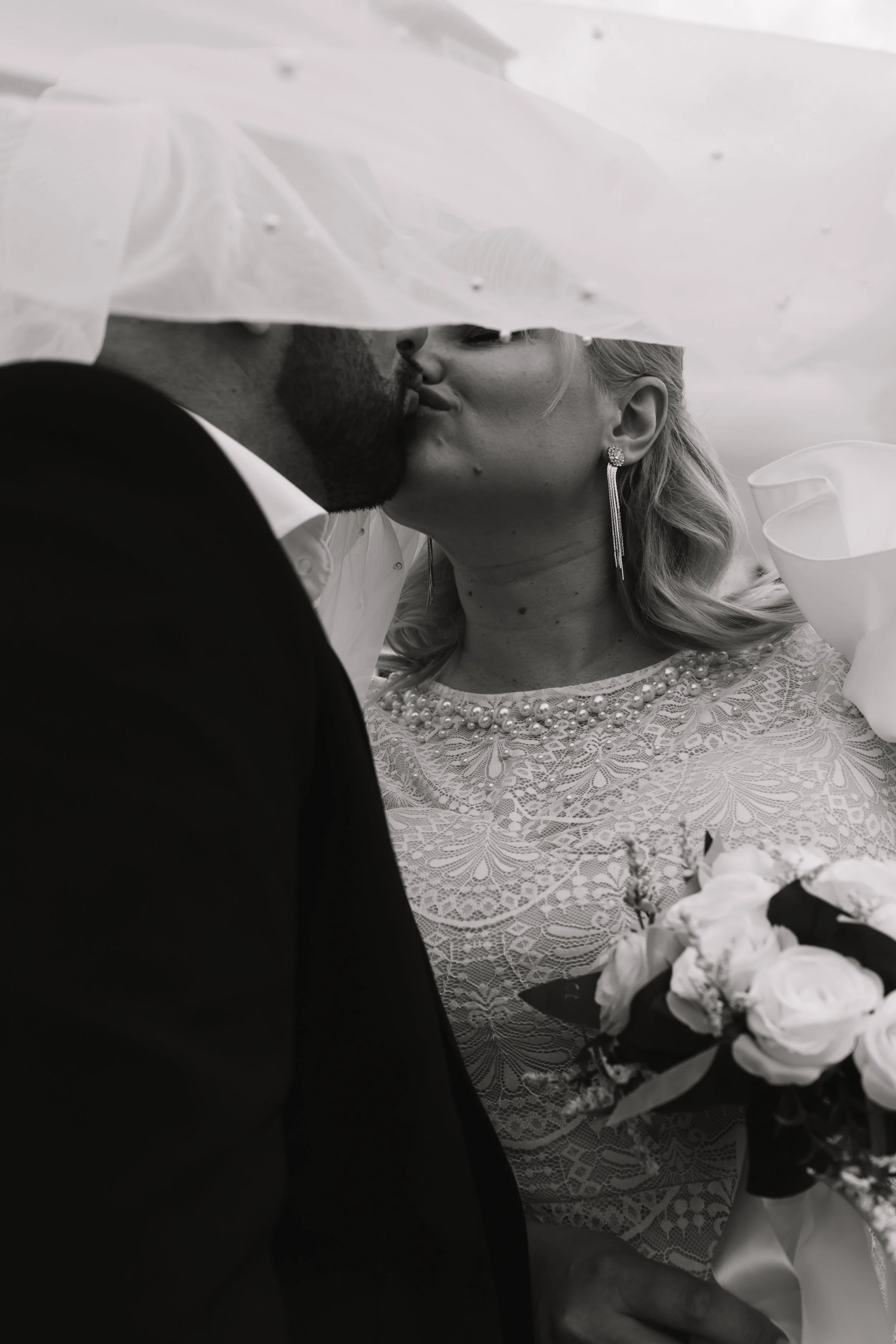 Braut und Bräutigam küssen sich unter einem Regenschirm bei ihrer Hochzeit.