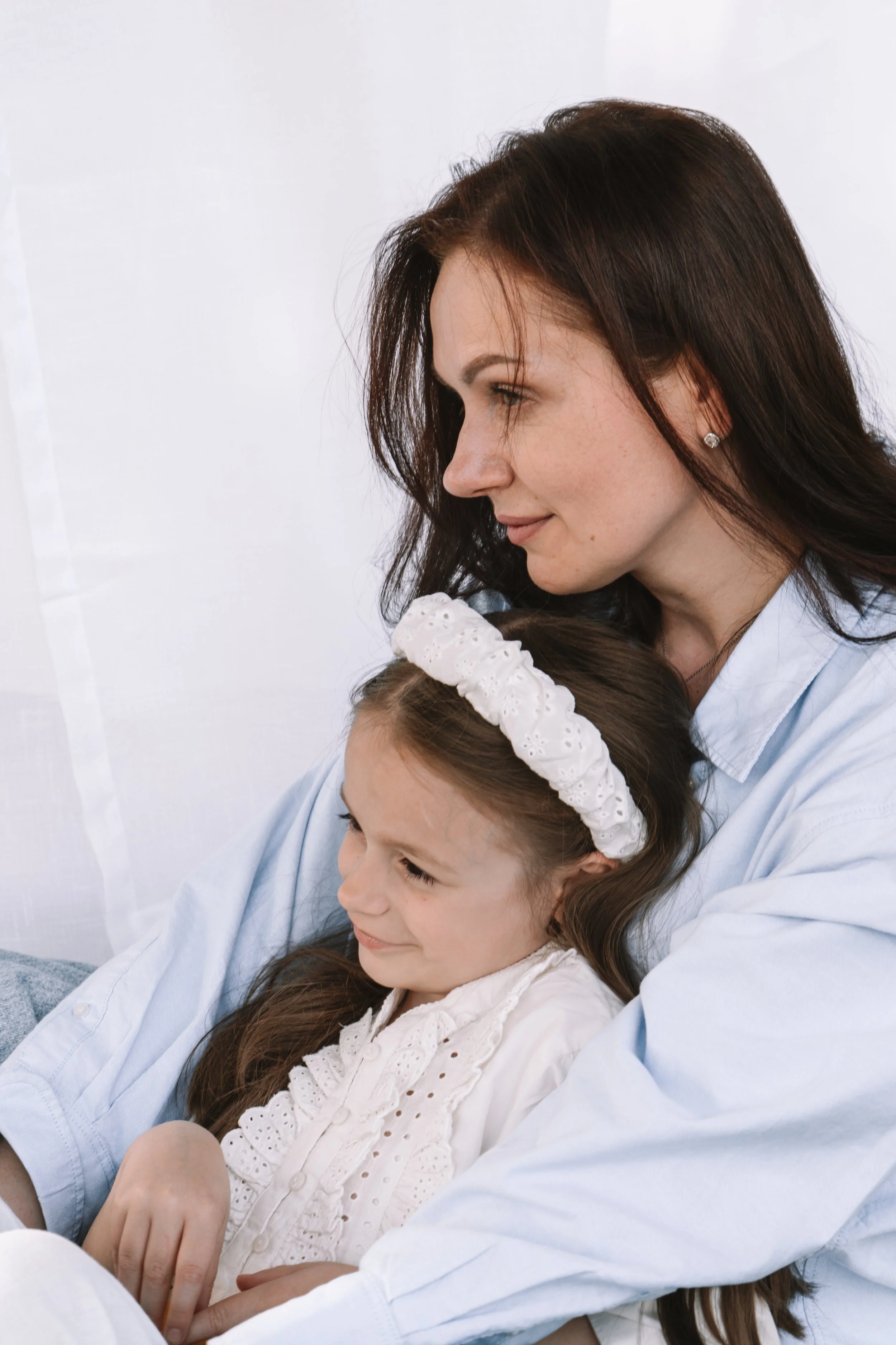 Eine Frau mit braunen, langem Haar hält ein lachendes Mädchen mit braunen Haaren und einem weißen Stirnband in den Armen.