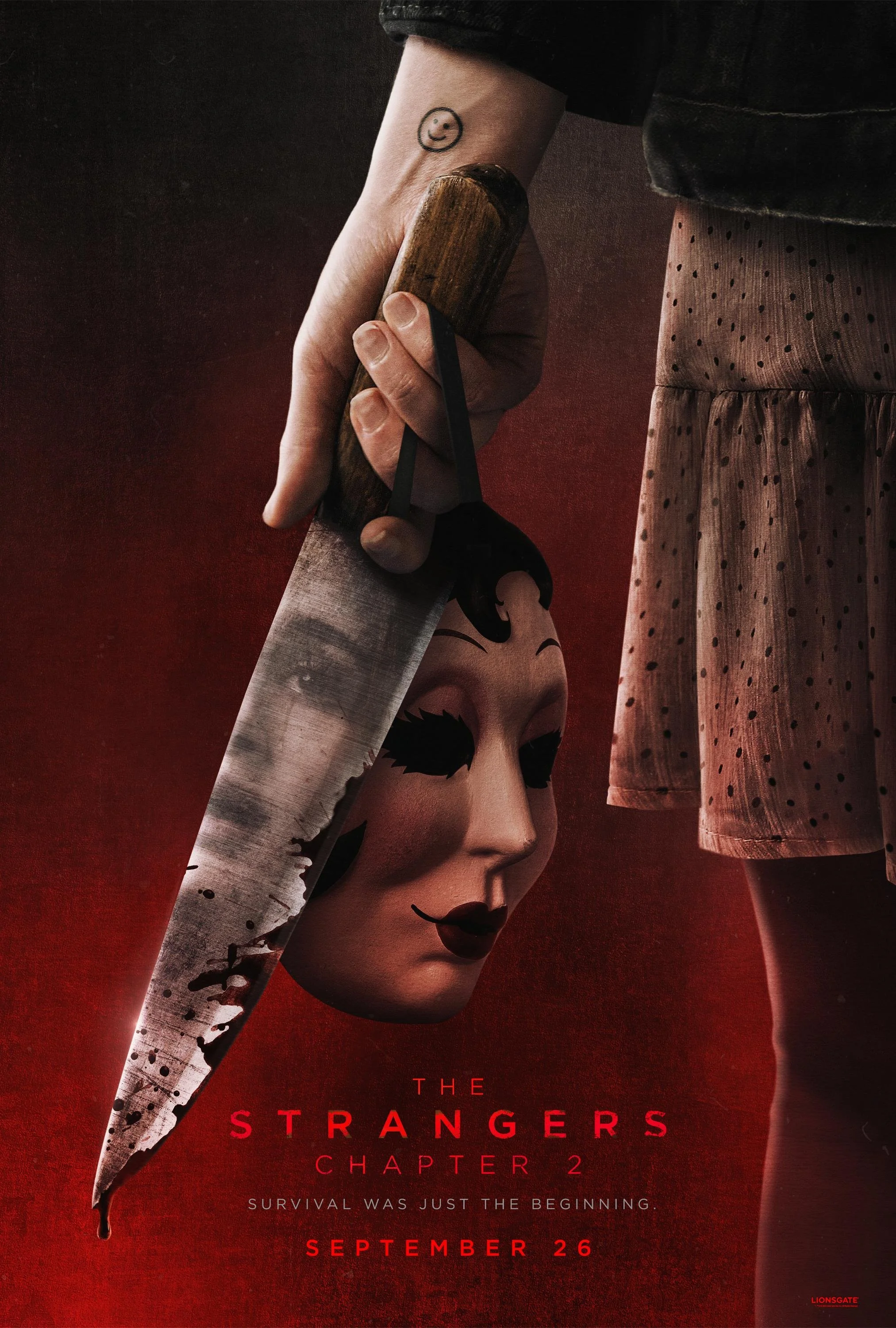A person holding a large butcher knife with a smiling face mask hanging from it, against a dark red background. The person has a smiley face tattoo on their wrist and is wearing a polka dot skirt.