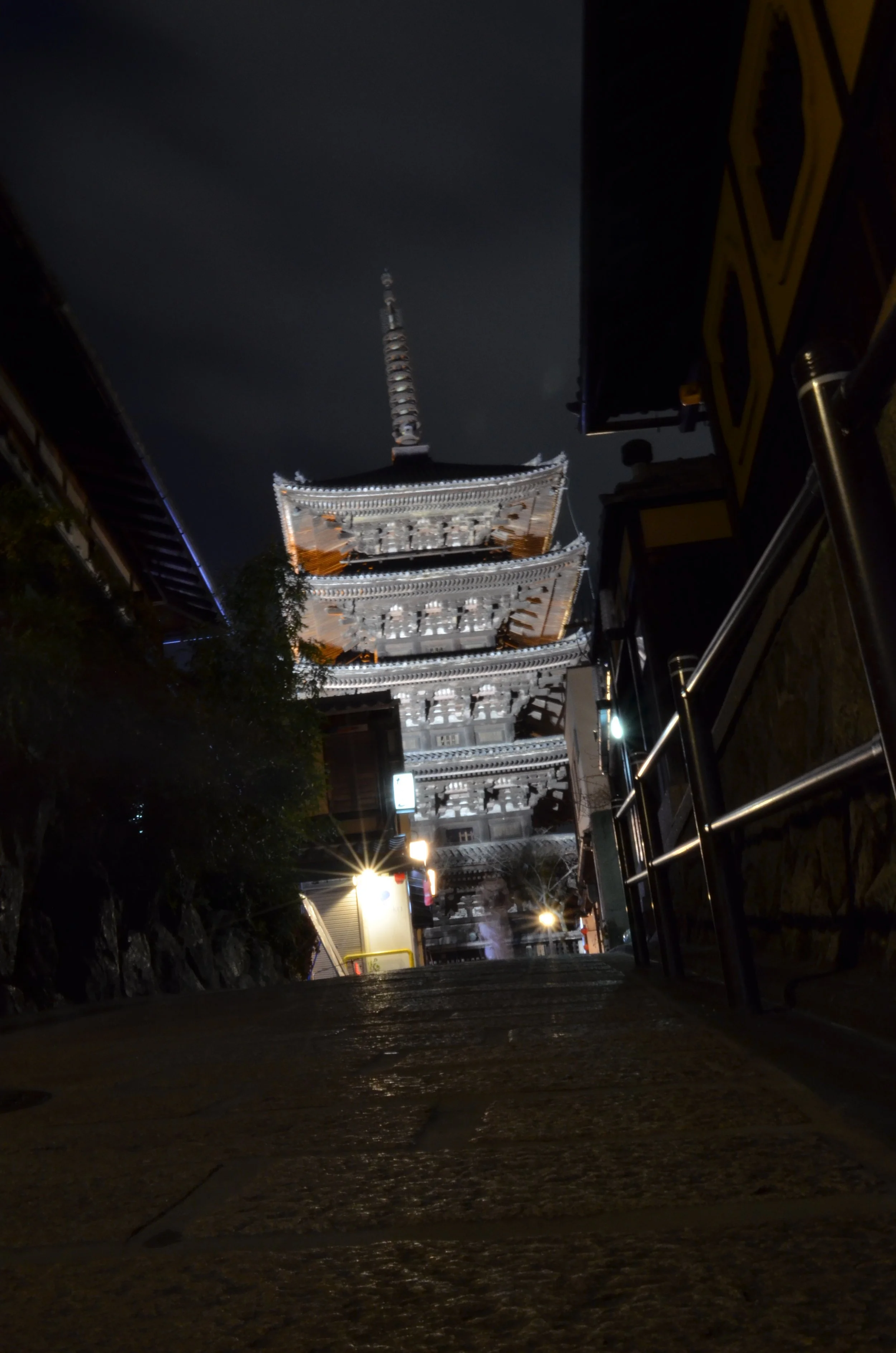 Una pagoda japonesa iluminada en la noche, vista desde abajo a lo largo de un camino.