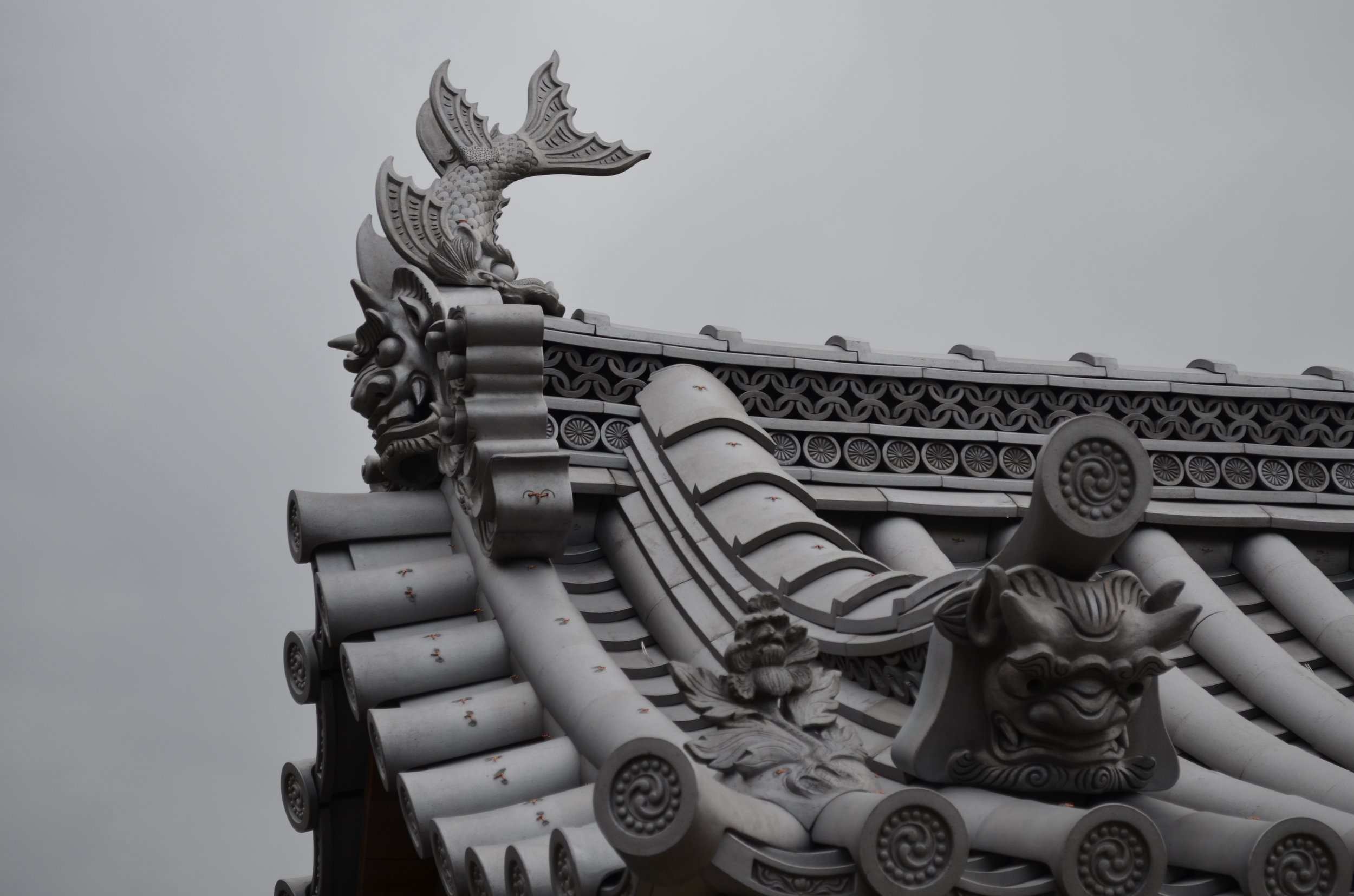 Detalles de la estructura del techo de un templo tradicional, con adornos de carvales y figuras de dragones y criaturas fantásticas en color gris.
