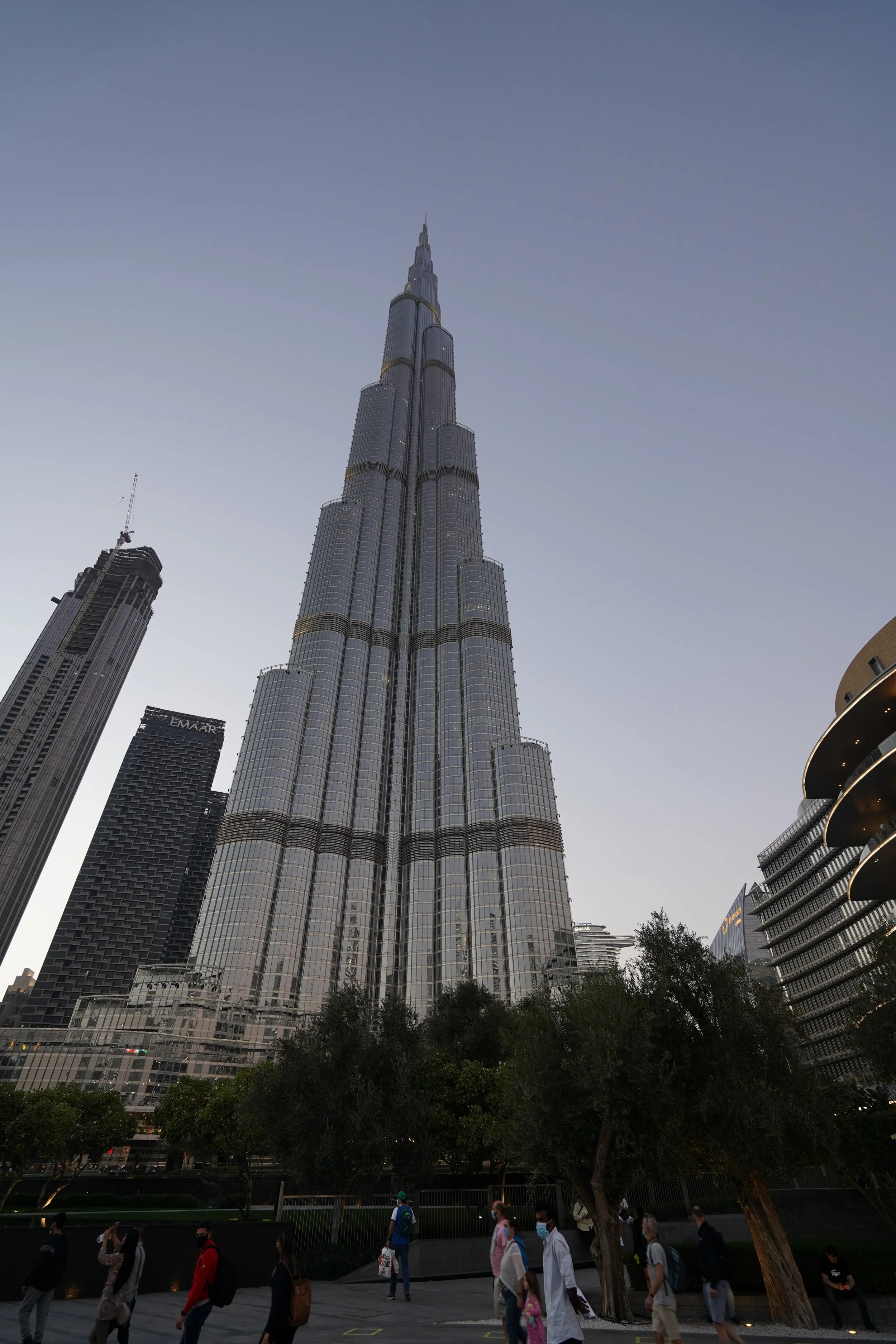 El edificio Burj Khalifa en Dubái visto desde abajo, con personas caminando en primer plano y algunos árboles debajo del edificio