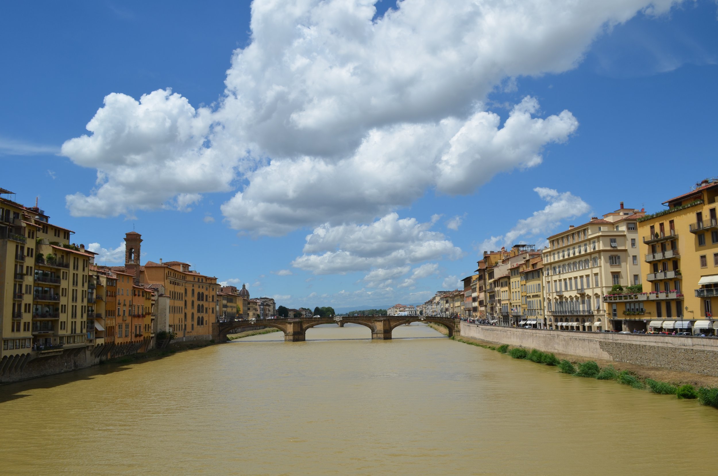 Vista del río Arno en Florencia, Italia, con puentes y edificios históricos a ambos lados, cielo con nubes grandes.