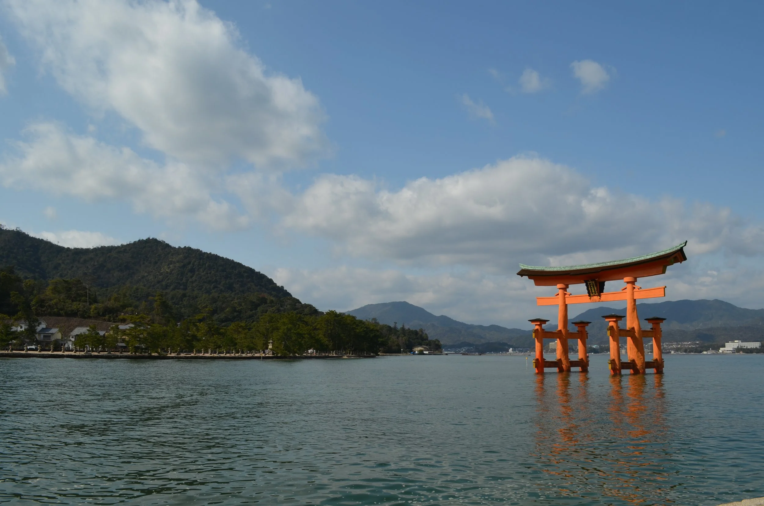 Torii japonés en el agua con montañas de fondo y cielo con nubes.