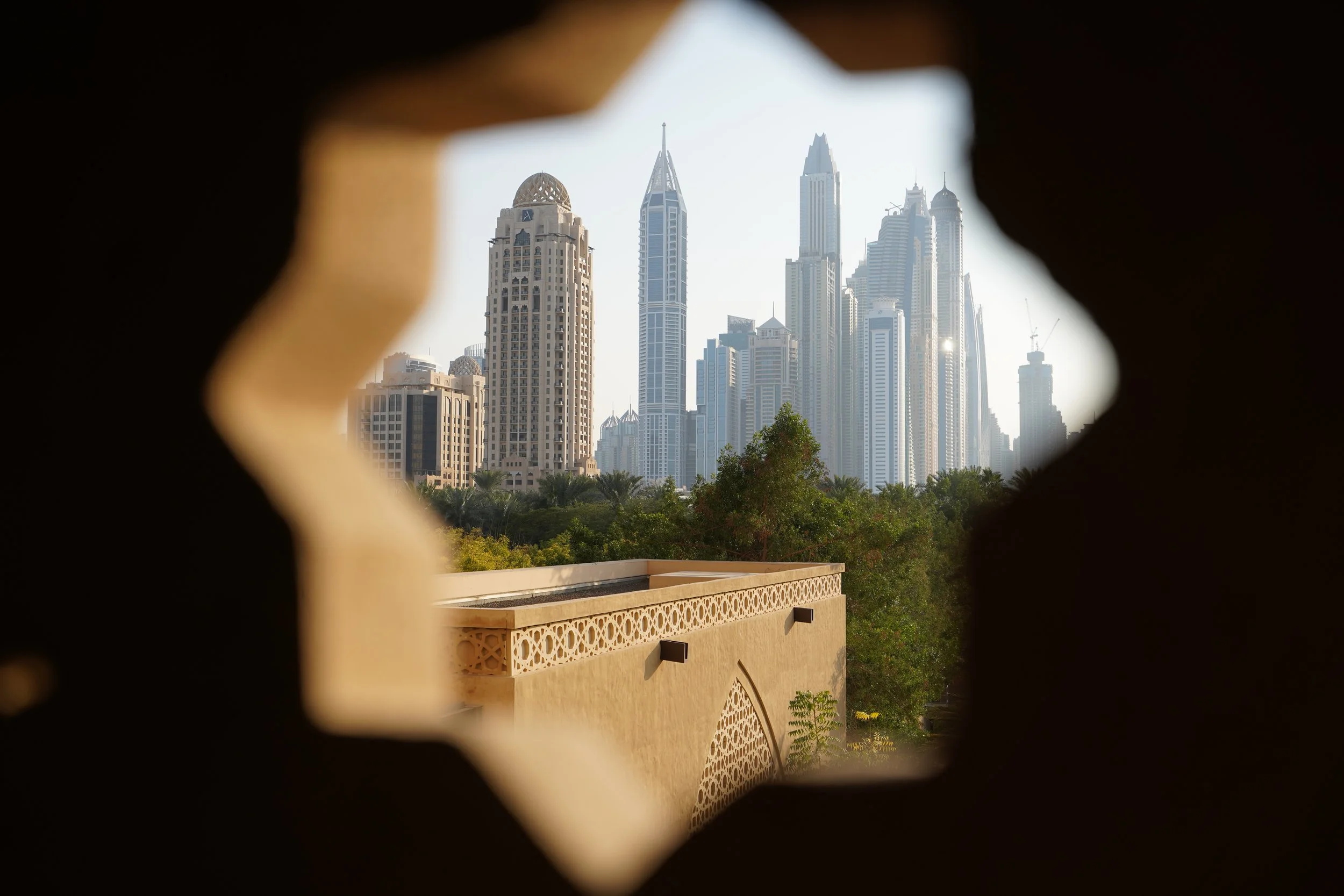 Vista de rascacielos en Dubái a través de un marco en forma de estrella, con jardines y estructura de estilo árabe en primer plano.