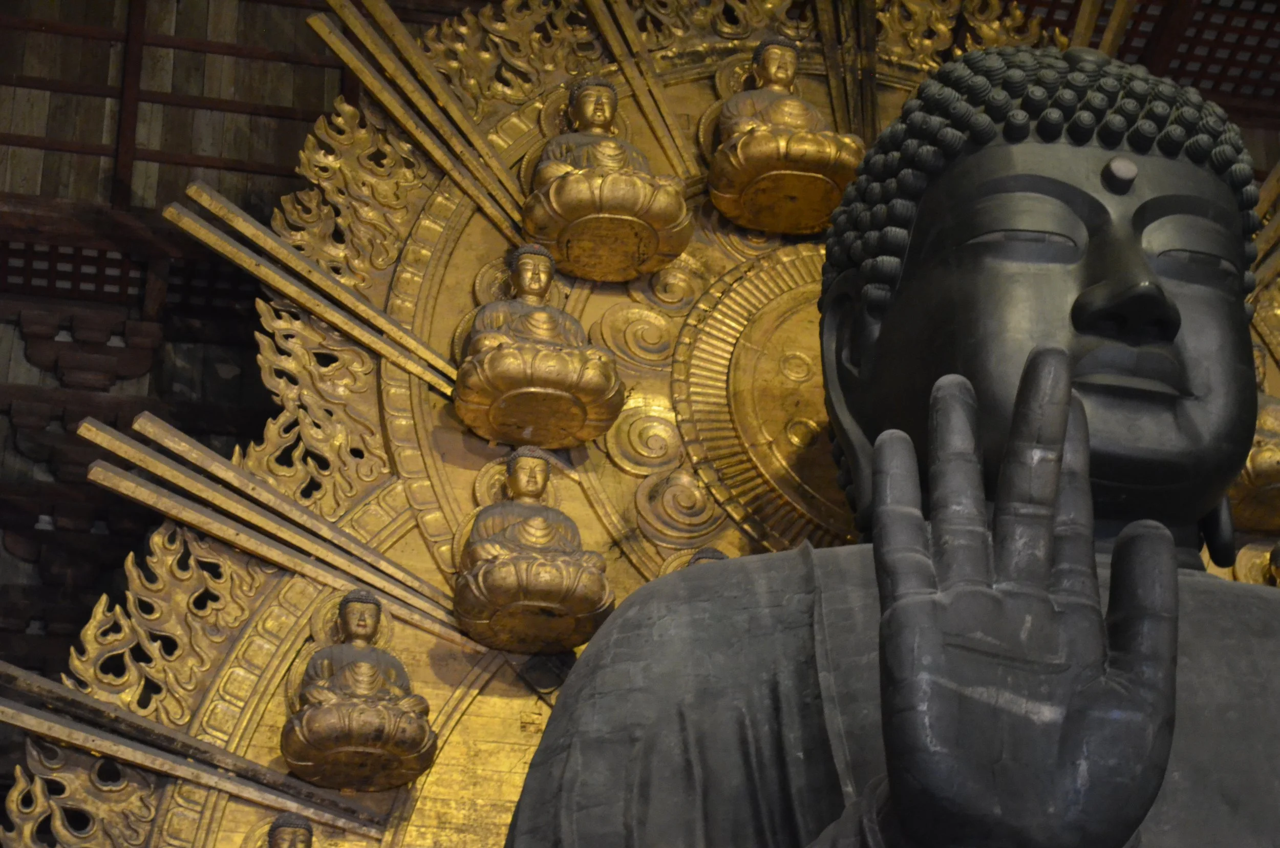Estatua gigante de Buda con mano en posición de mudra en un templo con decoraciones doradas y pequeñas figuras de Buda en el techo.