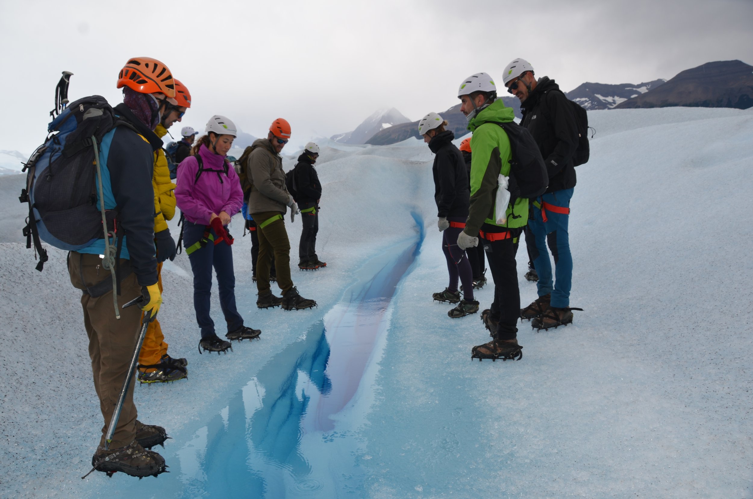 Grupo de personas haciendo senderismo en un glaciar, usando cascos y equipo de seguridad, observando una grieta en el hielo.