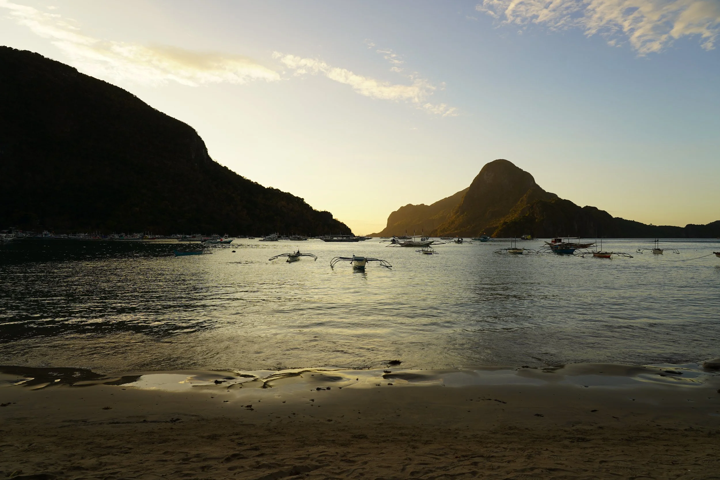 Atardecer en una playa con montañas y barcos en el agua