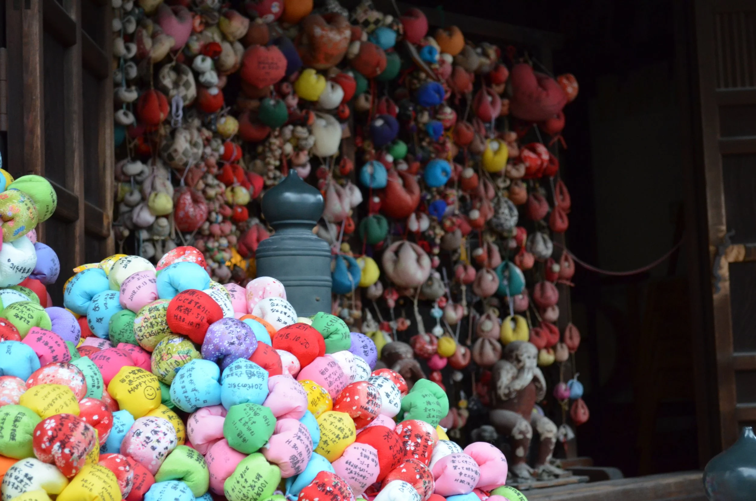 Exposición de amuletos y objetos tradicionales de colores en un mercado o tienda, con muchos colgados en el fondo y en el frente en diversas formas y tamaños.