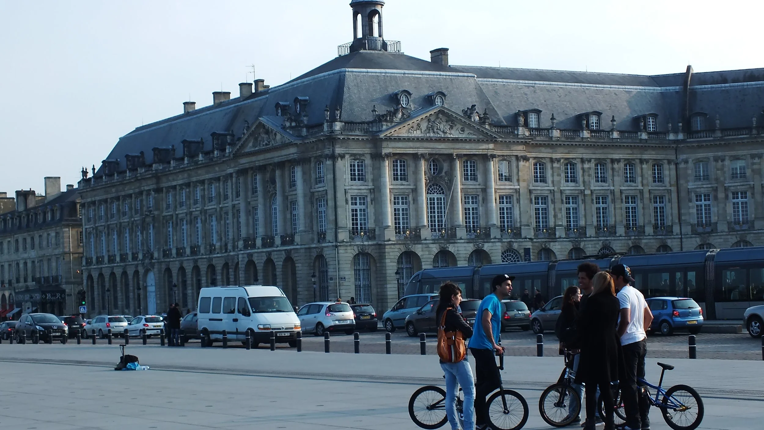 Grupo de jóvenes con bicicletas conversando en una plaza frente a un edificio histórico en París.
