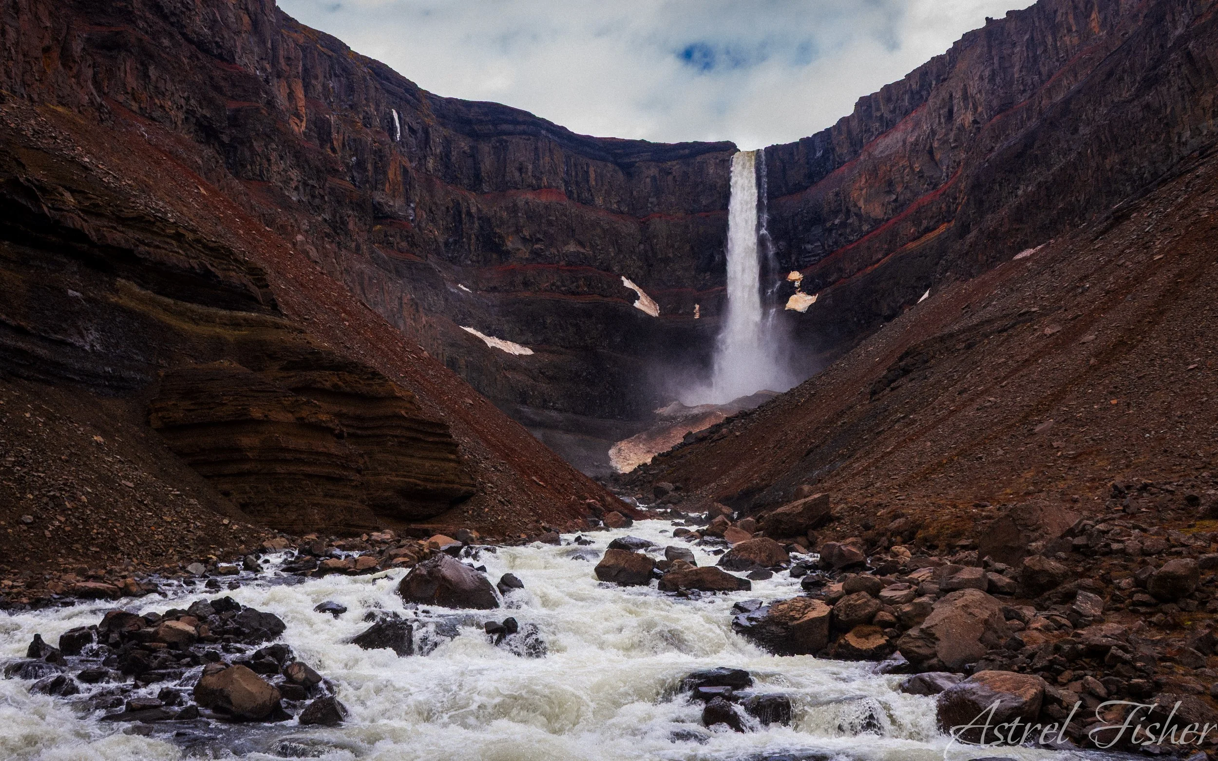 A waterfall cascading down a rocky cliff into a river rushing through a canyon.
