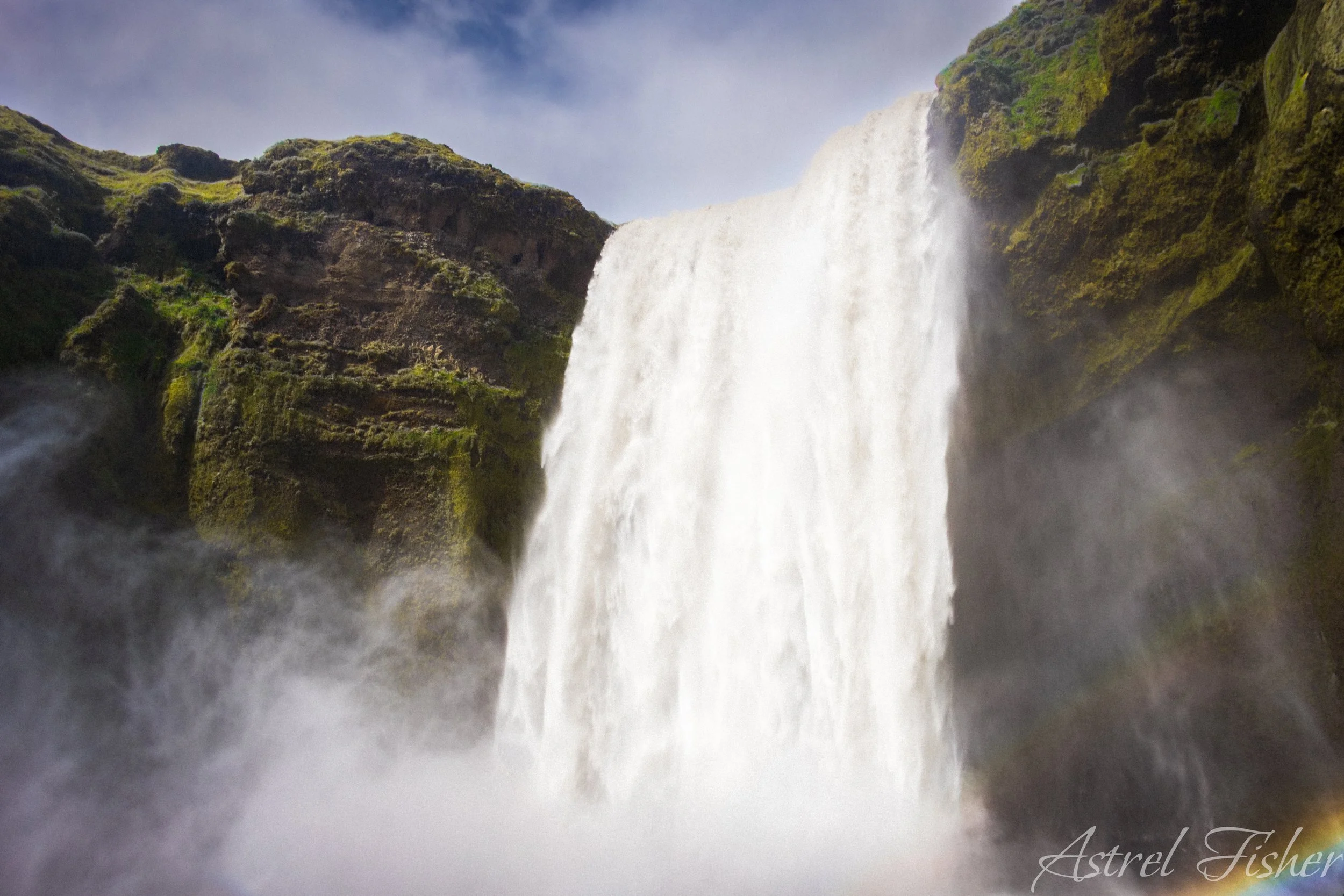 A large waterfall cascading down rocky cliffs covered in green moss.