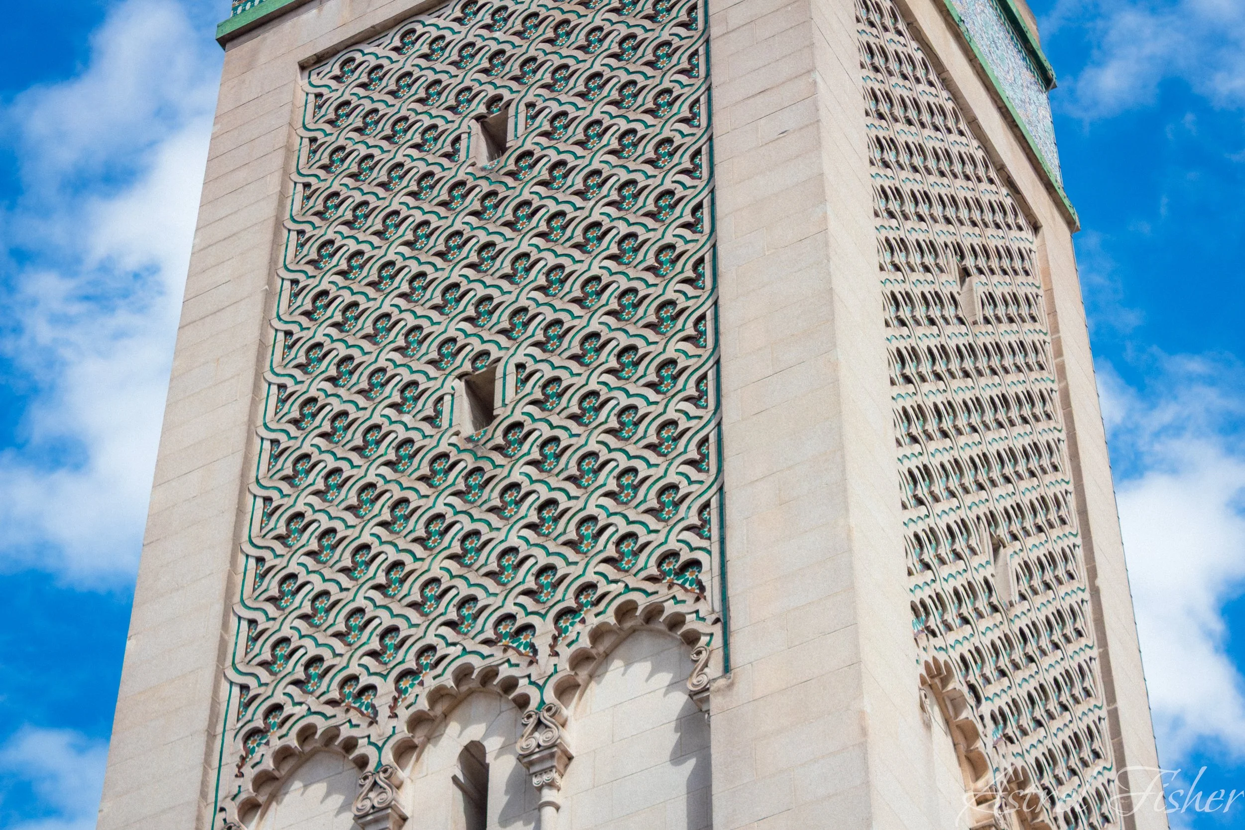 Close-up of a tall building with intricate art deco architectural details and decorative tile work, set against a blue sky with some clouds.
