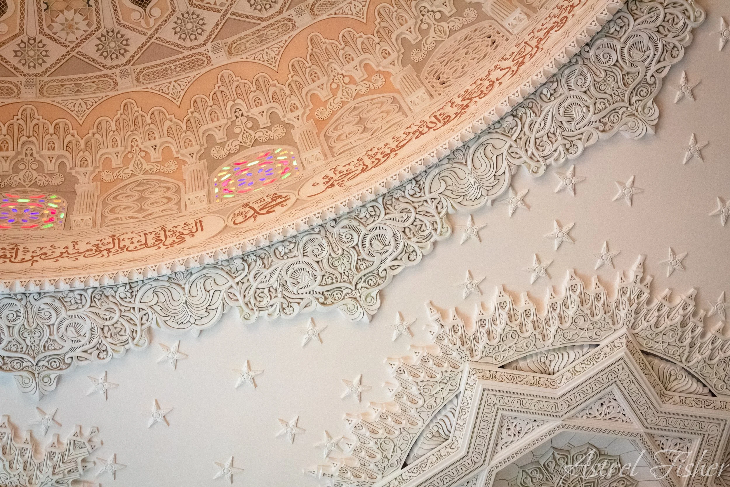Intricate white carved arch with Arabic script and colorful stained glass interior