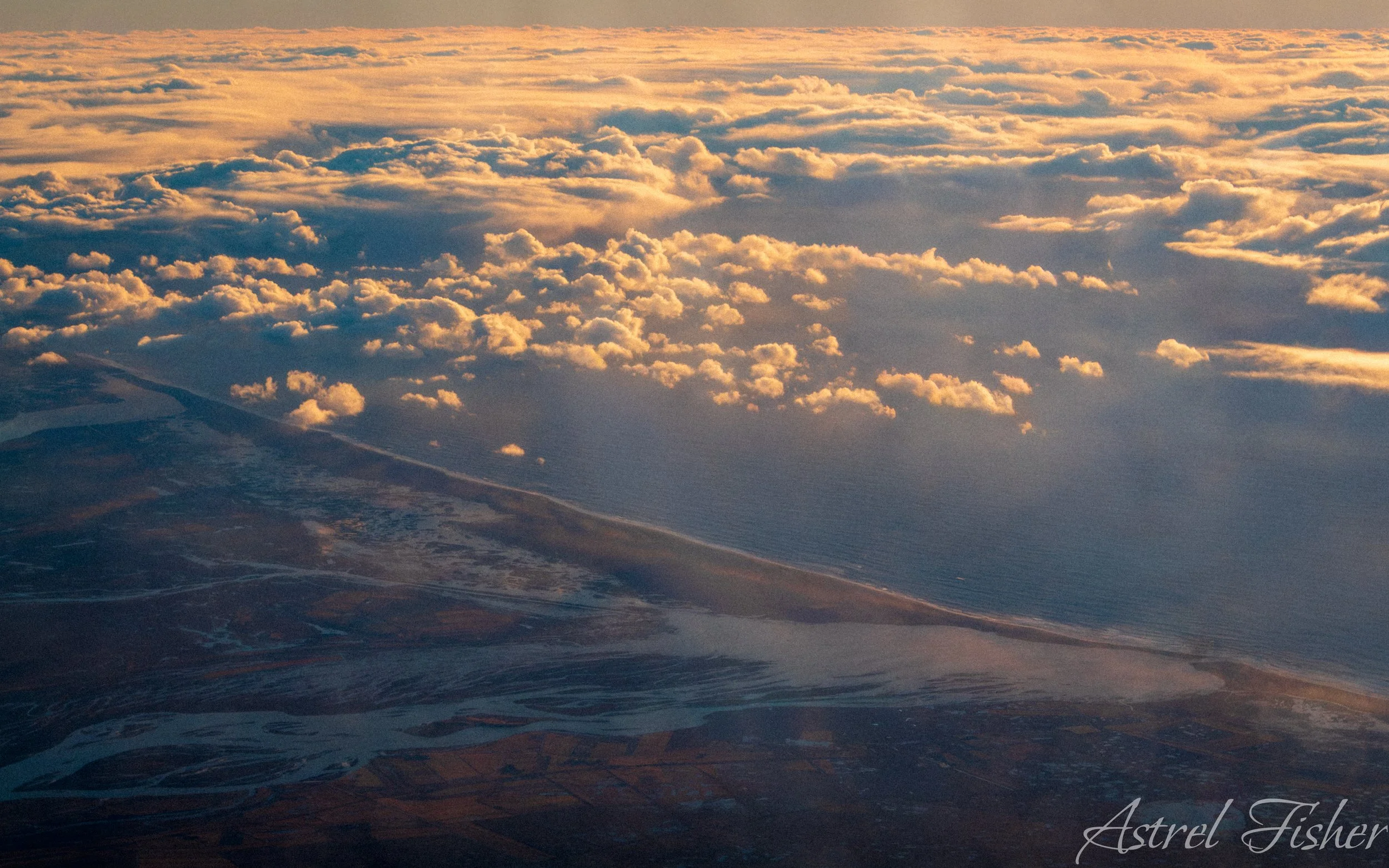 Aerial view of clouds during sunset or sunrise over a landscape with water and land.