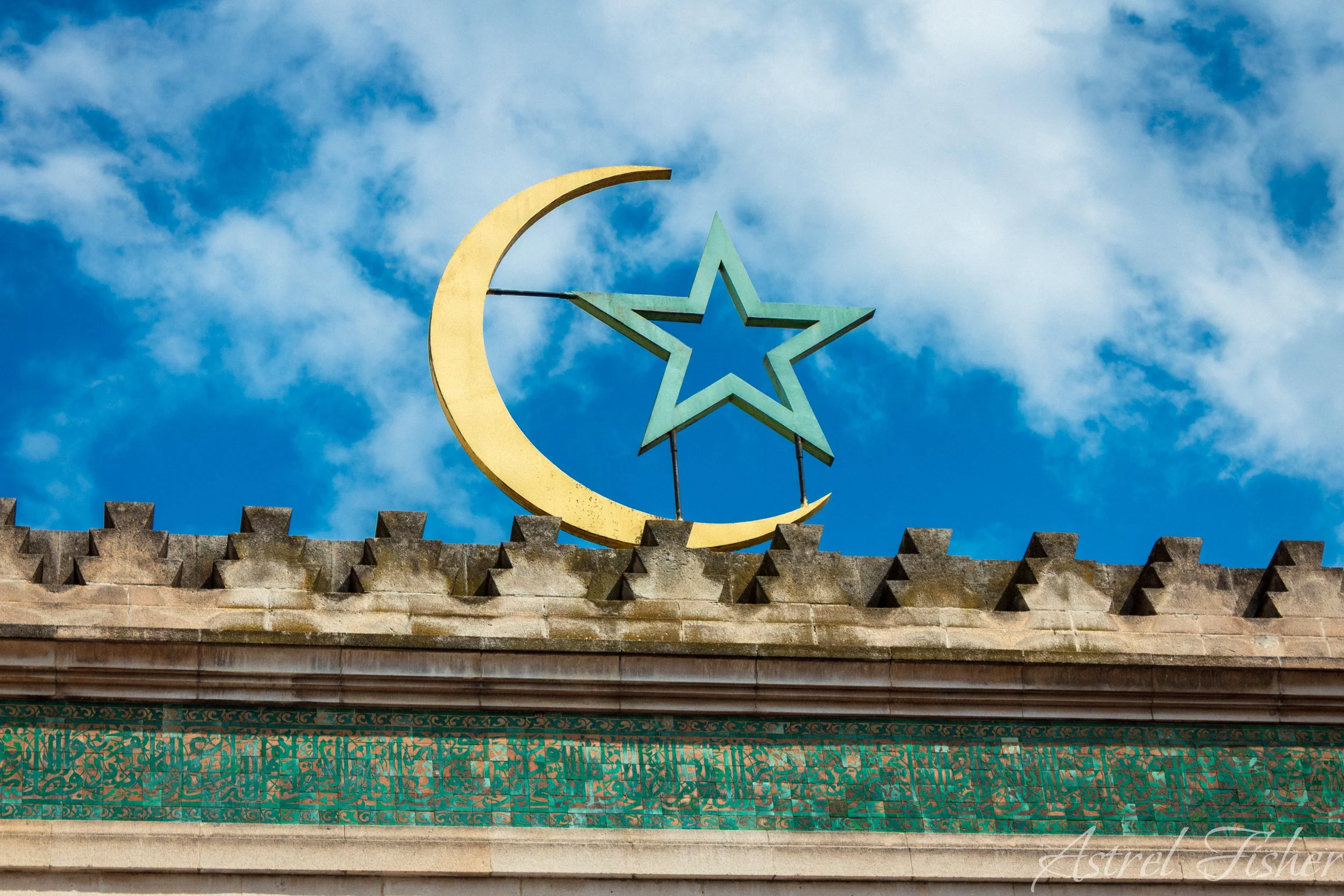 Close-up of a building's roof with a golden crescent moon and star symbol on top, set against a blue sky with clouds.