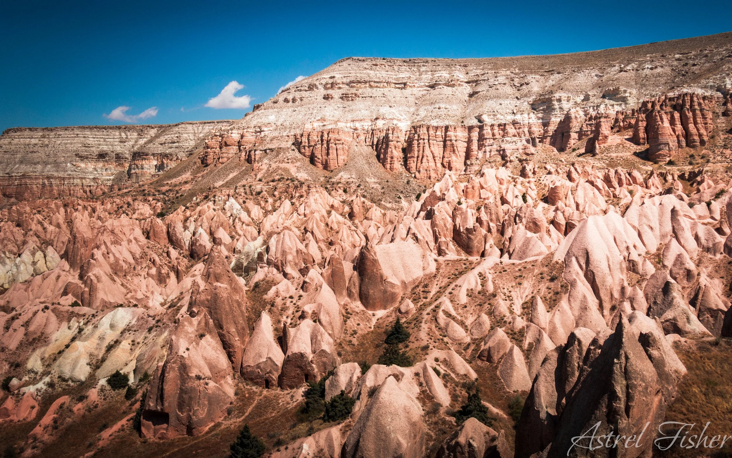 Colorful layered rock formations in a desert landscape under a blue sky with a few clouds.