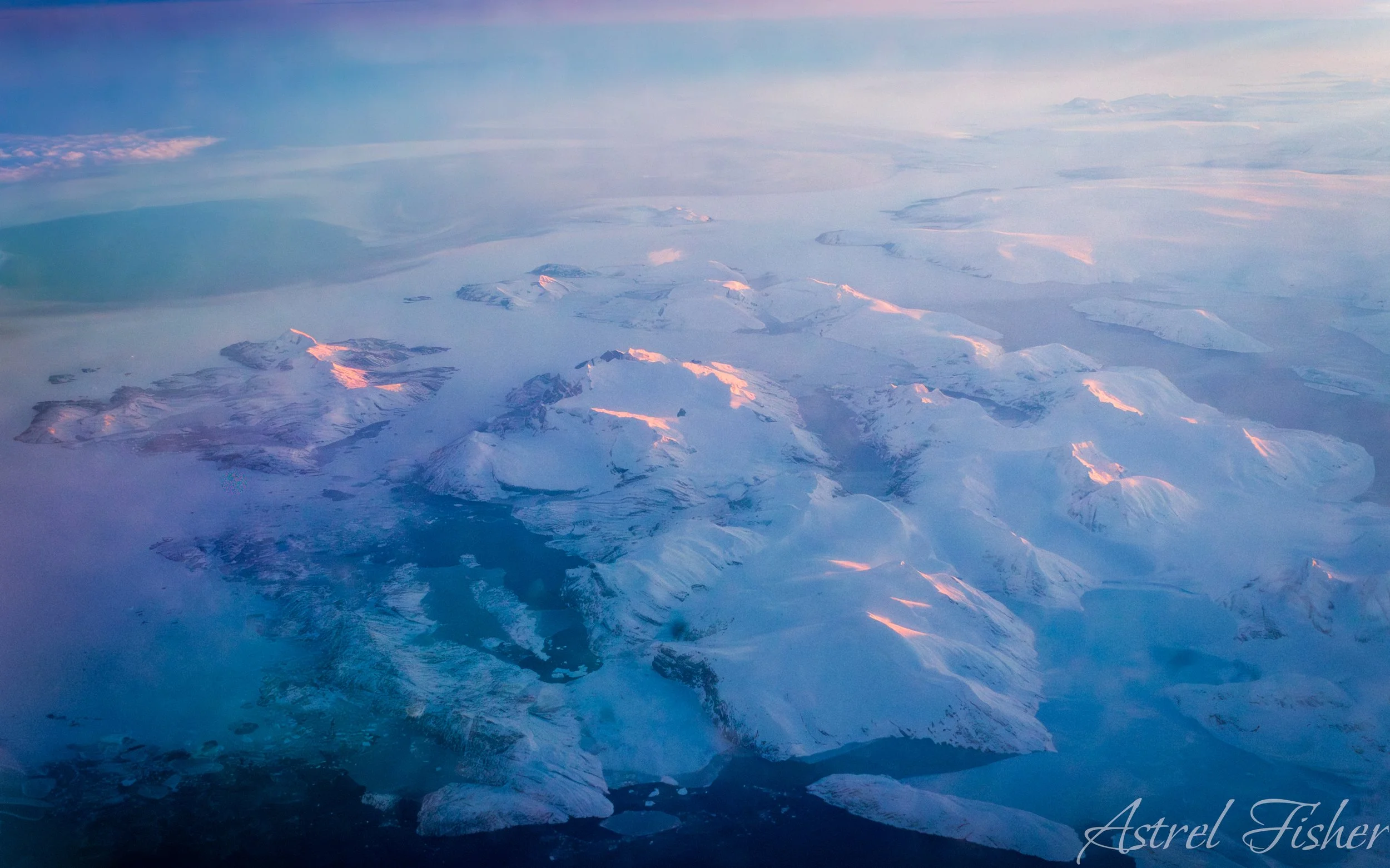 Aerial view of snow-covered mountainous terrain with glaciers and icy landscape, illuminated by soft light.