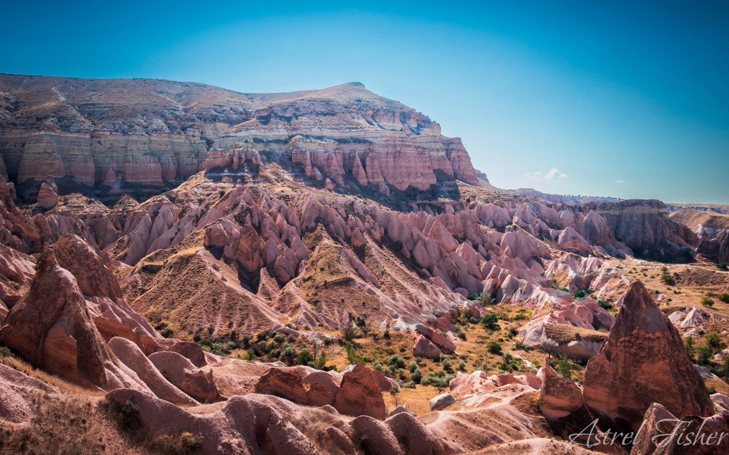 Colorful layered rock formations and hills under a clear blue sky.