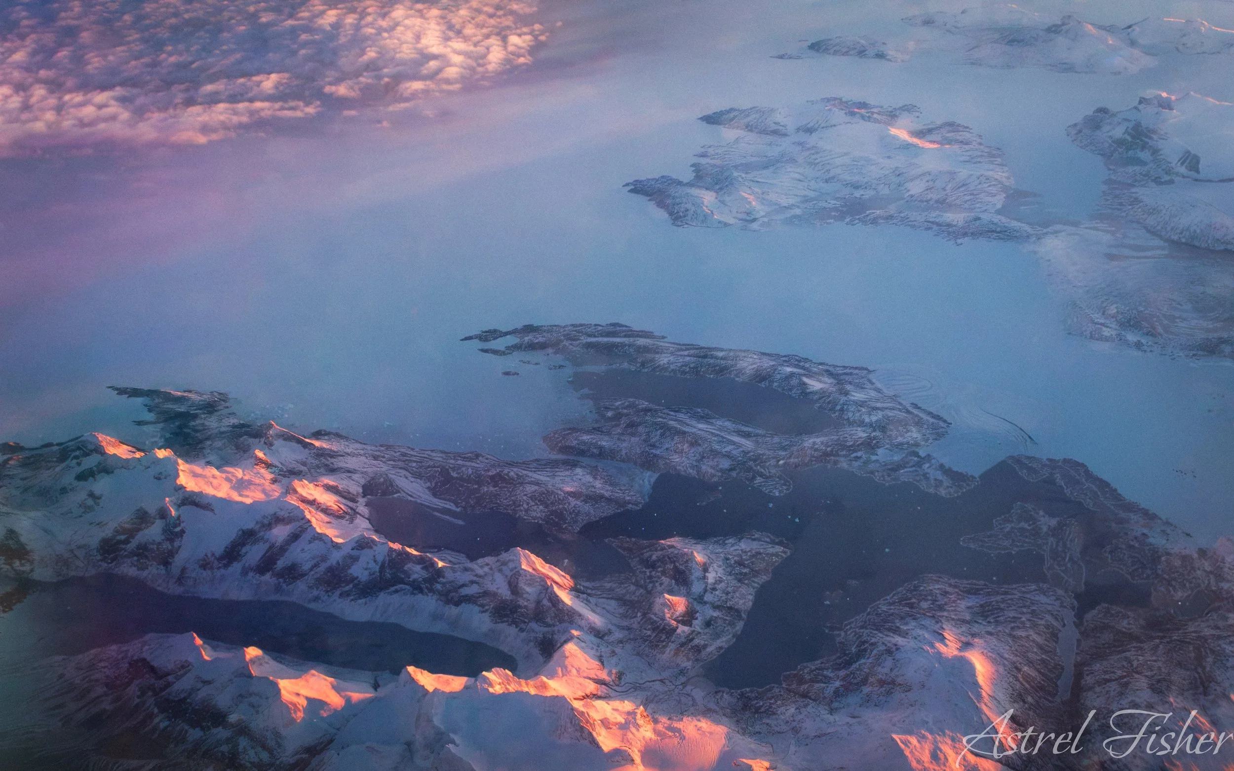 Aerial view of snowy mountain peaks with pink and purple sunset sky.