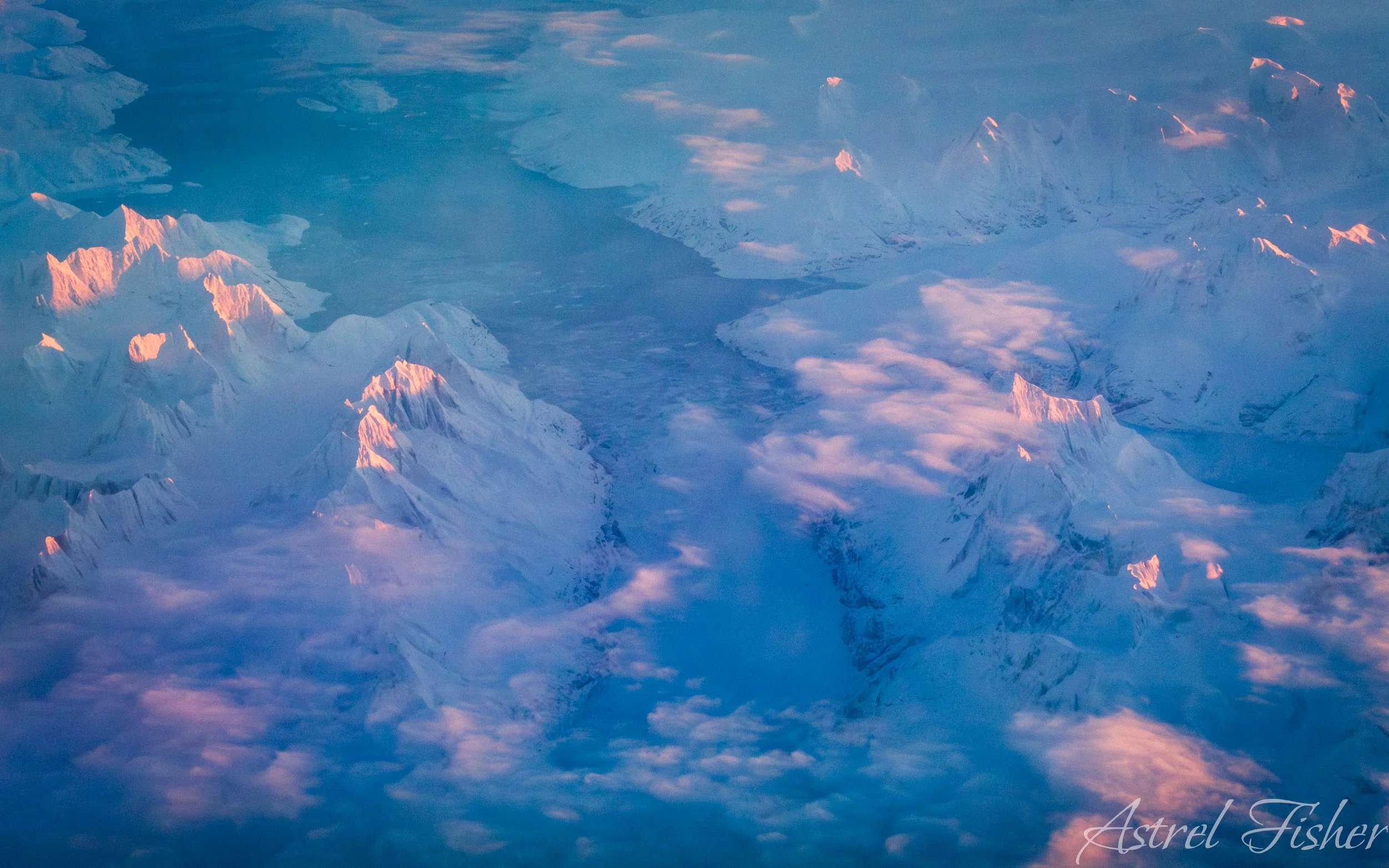 Aerial view of snow-covered mountains at sunset, with pink and blue hues in the sky.