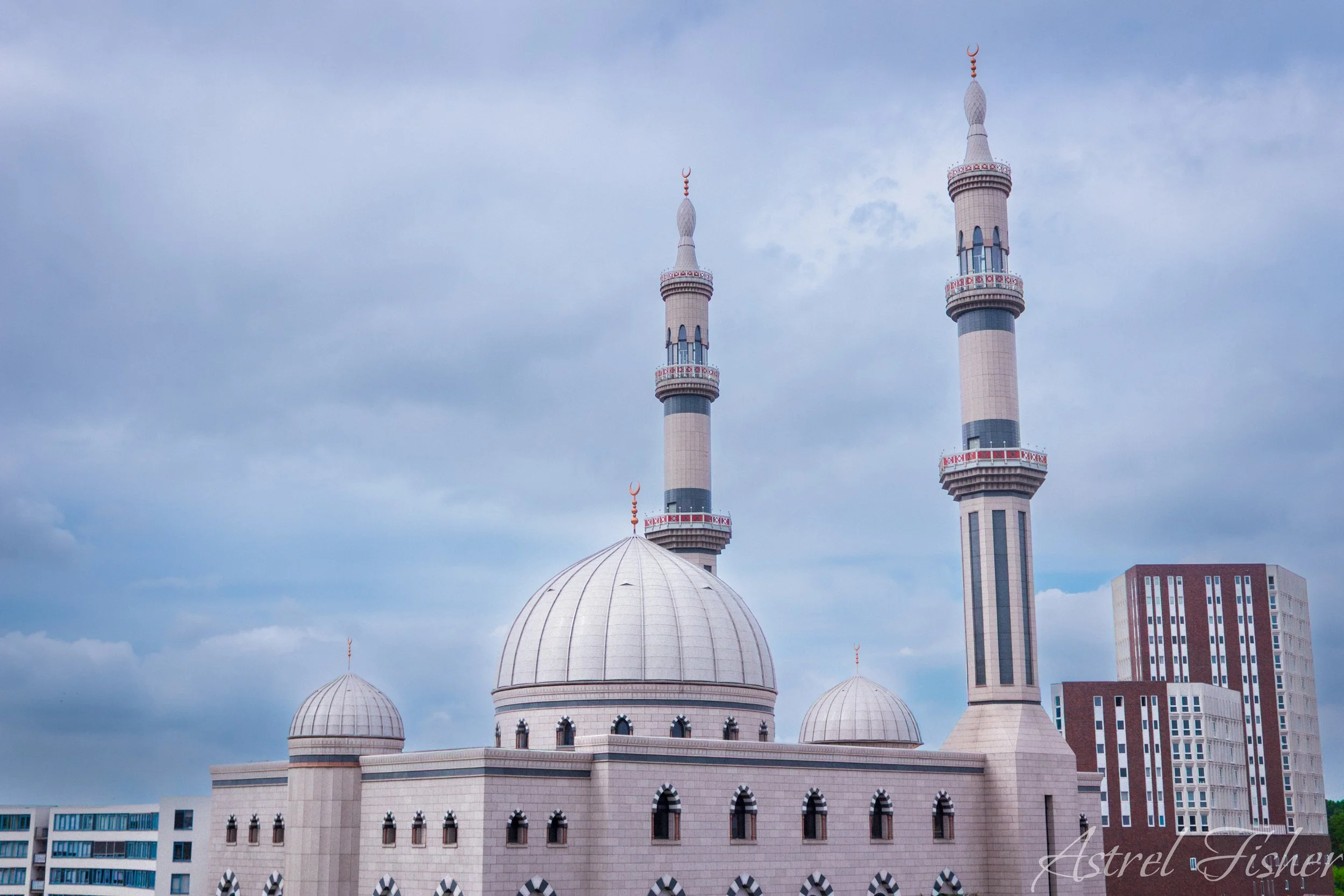 A mosque with multiple domes and two tall minarets against a partly cloudy sky.