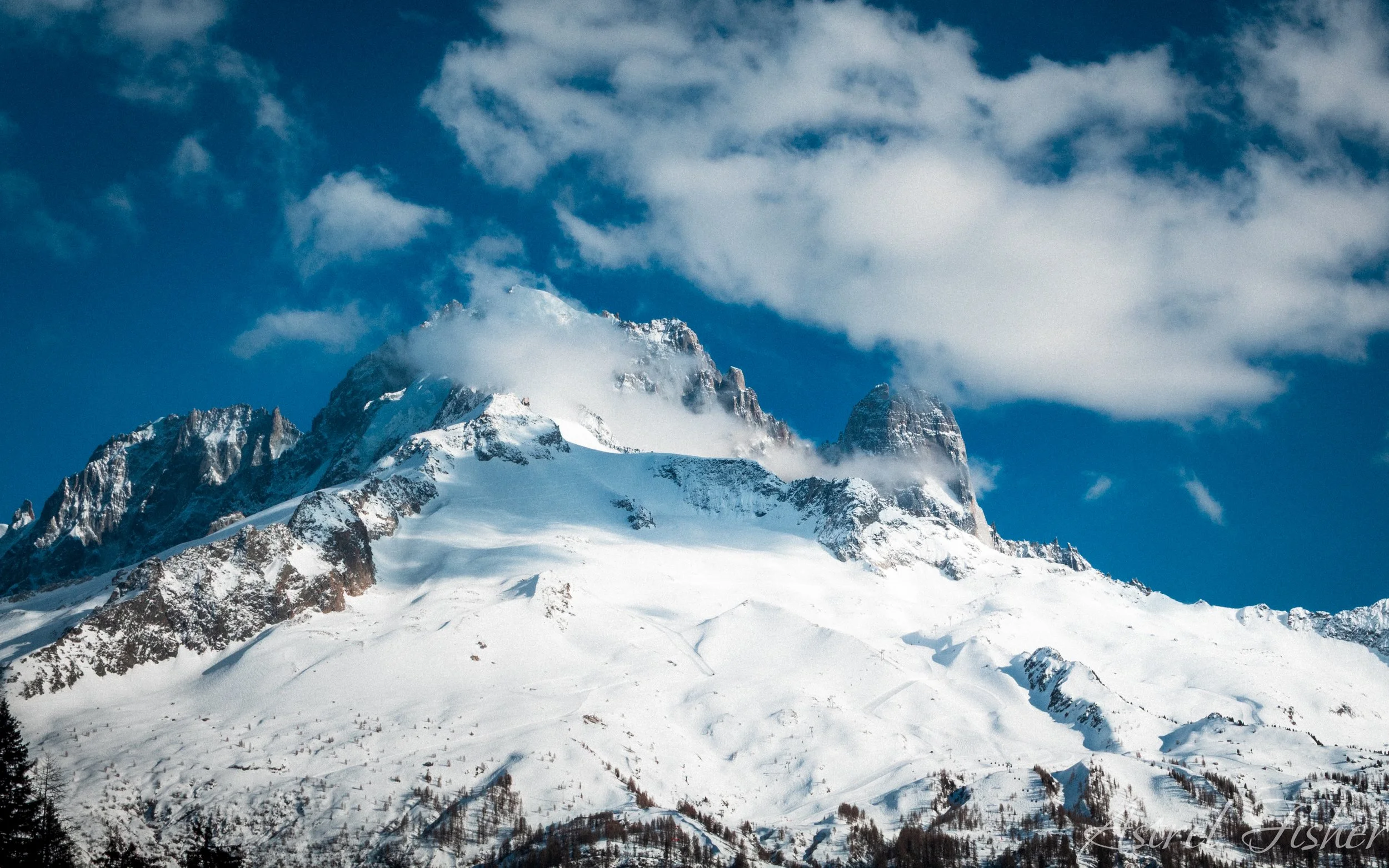 Snow-covered mountain peaks with a blue sky and some clouds.
