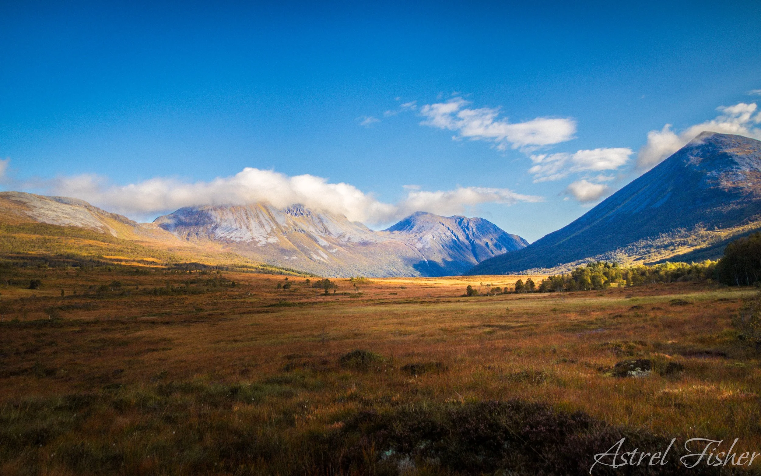 Scenic landscape of mountains with partly cloudy sky, green and brown vegetation in the foreground.