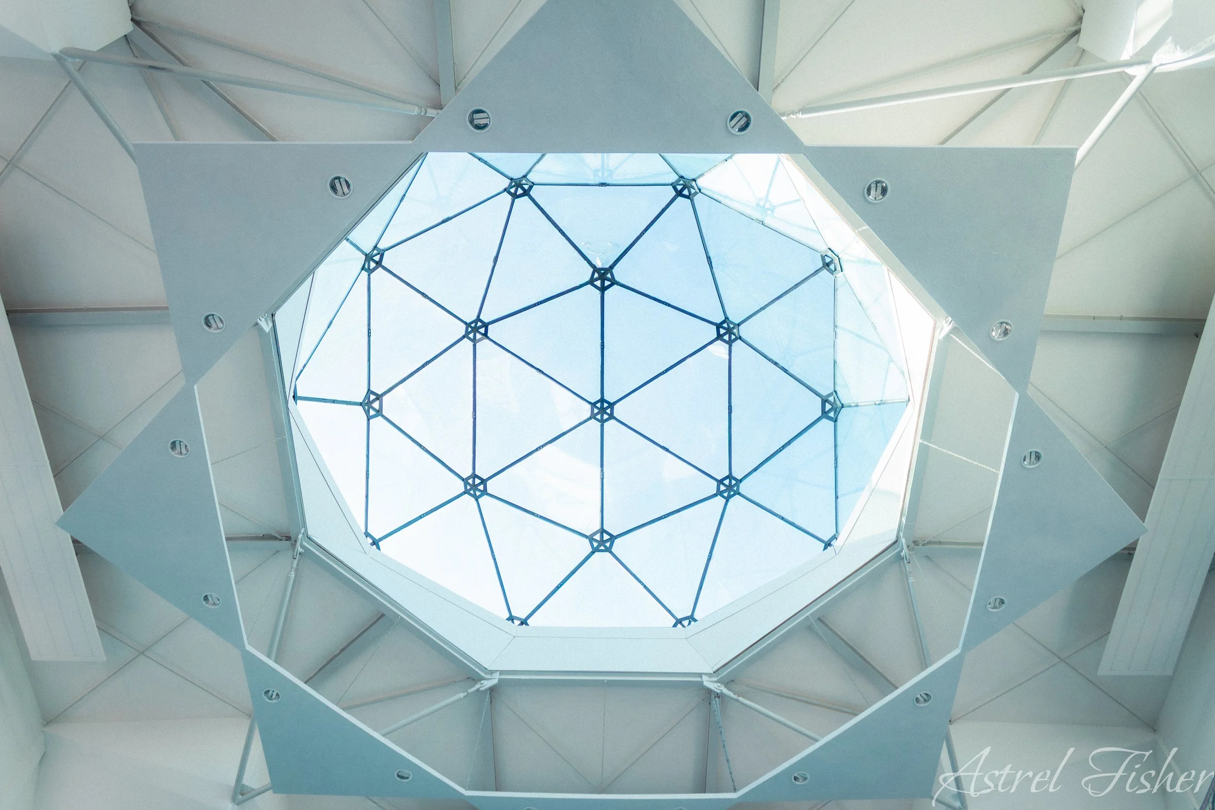 Looking up through an open ceiling with a geometric glass skylight surrounded by modern architectural white walls.